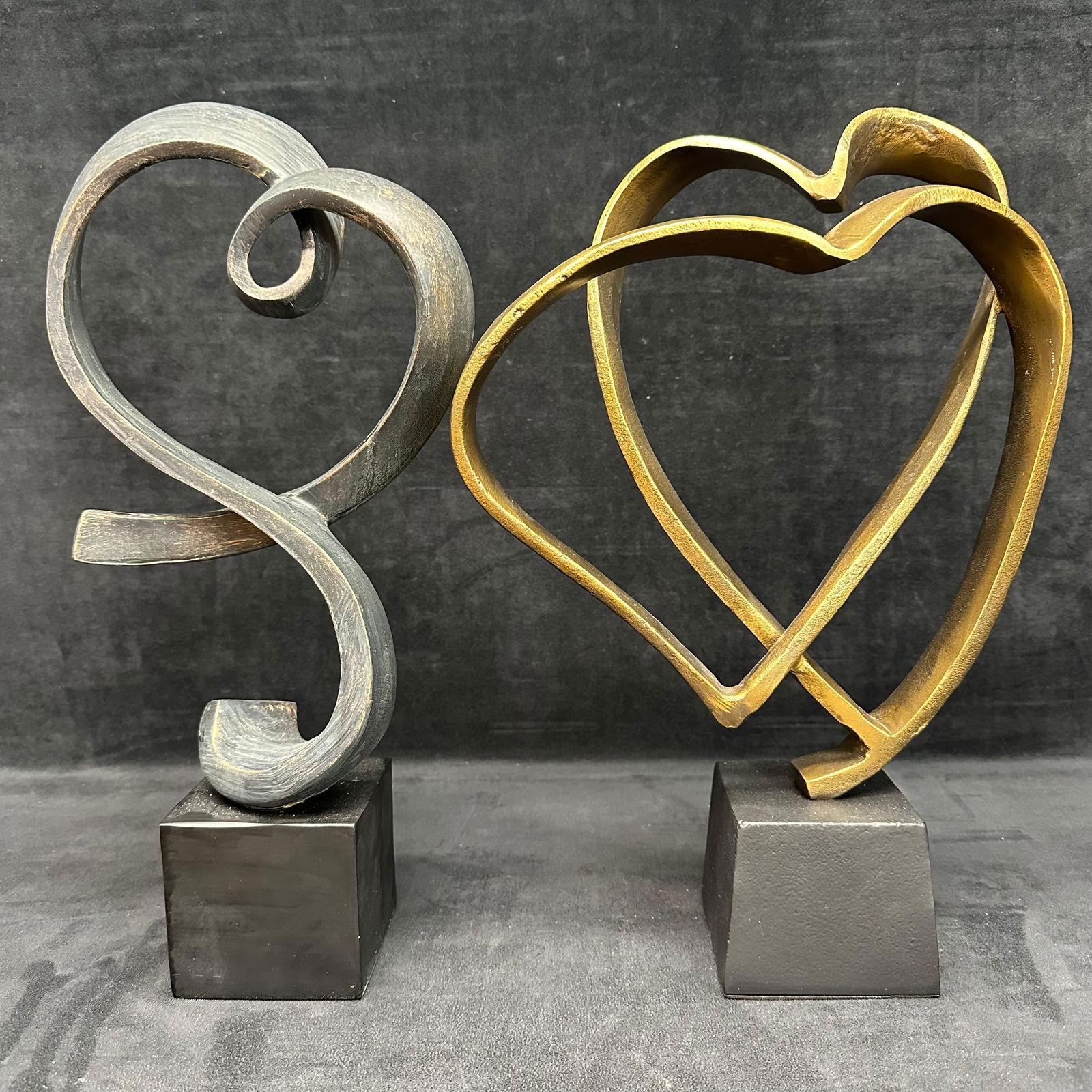 Pair of Modern Abstract Heart Sculptures on Bases: Pair of decorative modern abstract heart sculptures, one in bronze-tone finish and the other in a dark patinated metallic finish. Each piece features free-form heart-inspired designs mounted on sturdy