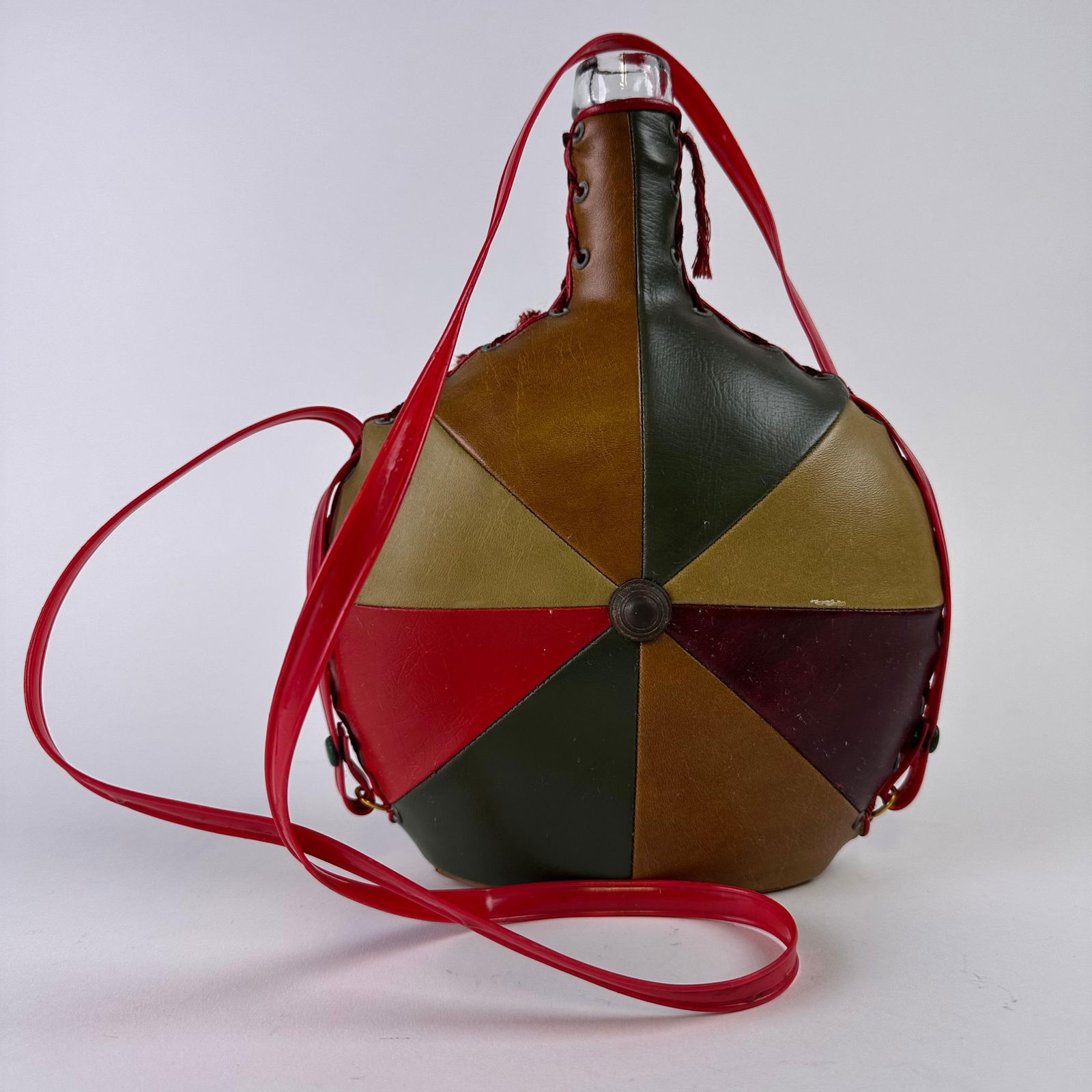 Vintage Multi Colored Leather Wrapped Glass Wine Flask Jug with Red Strap: Vintage multicolor leather-wrapped glass wine jug with red vinyl strap and lace-up sides. Features a geometric patchwork design with a central metal button accent. A great retro barware or decorative