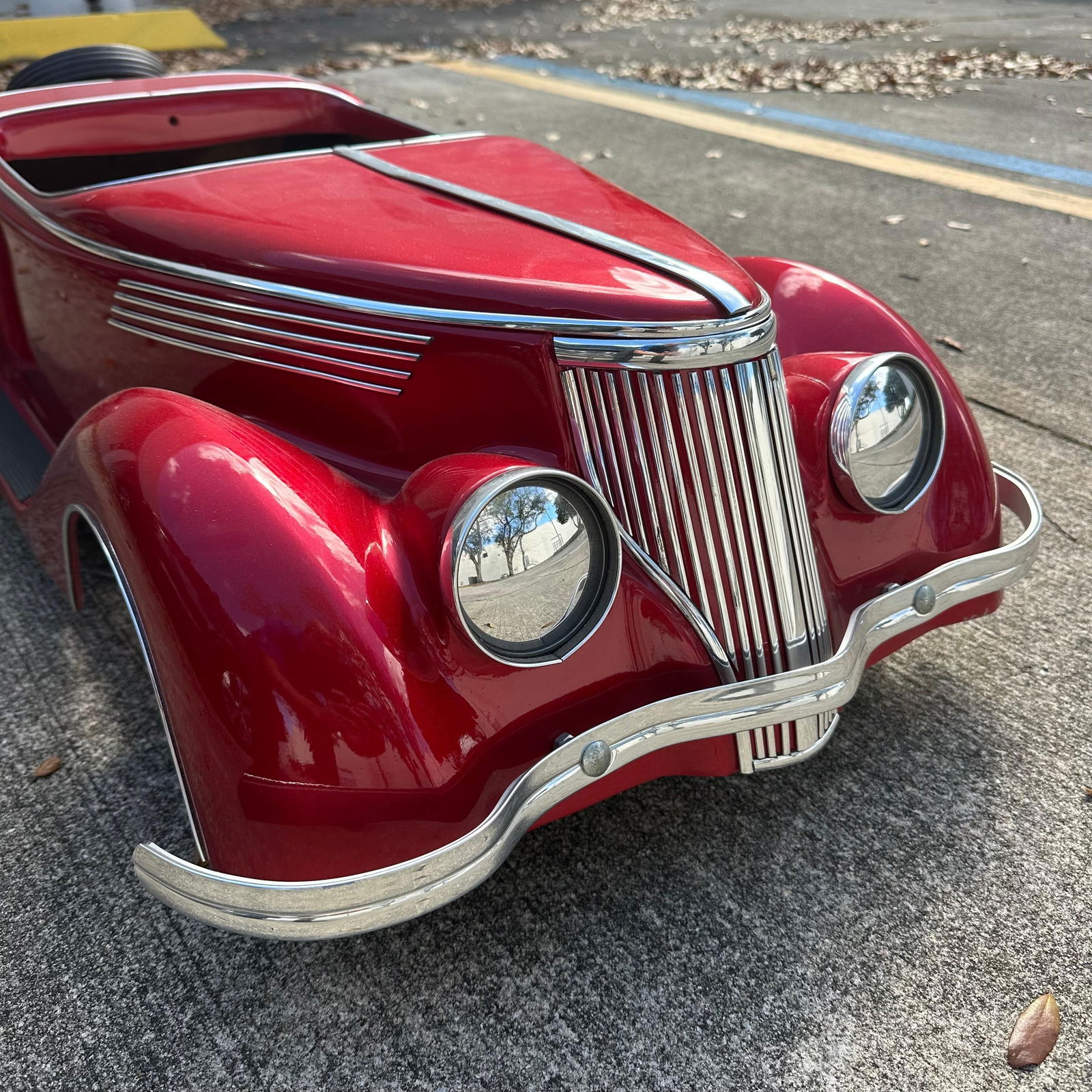 Custom Red Metal Pedal Car Spare Tire and Tufted Seat 1930s Roadster Style R118: Vintage custom metal pedal car styled after a 1930s roadster, finished in metallic red paint with chrome trim details. Features include a vertical grille with dual headlights, chrome bumper trim, side