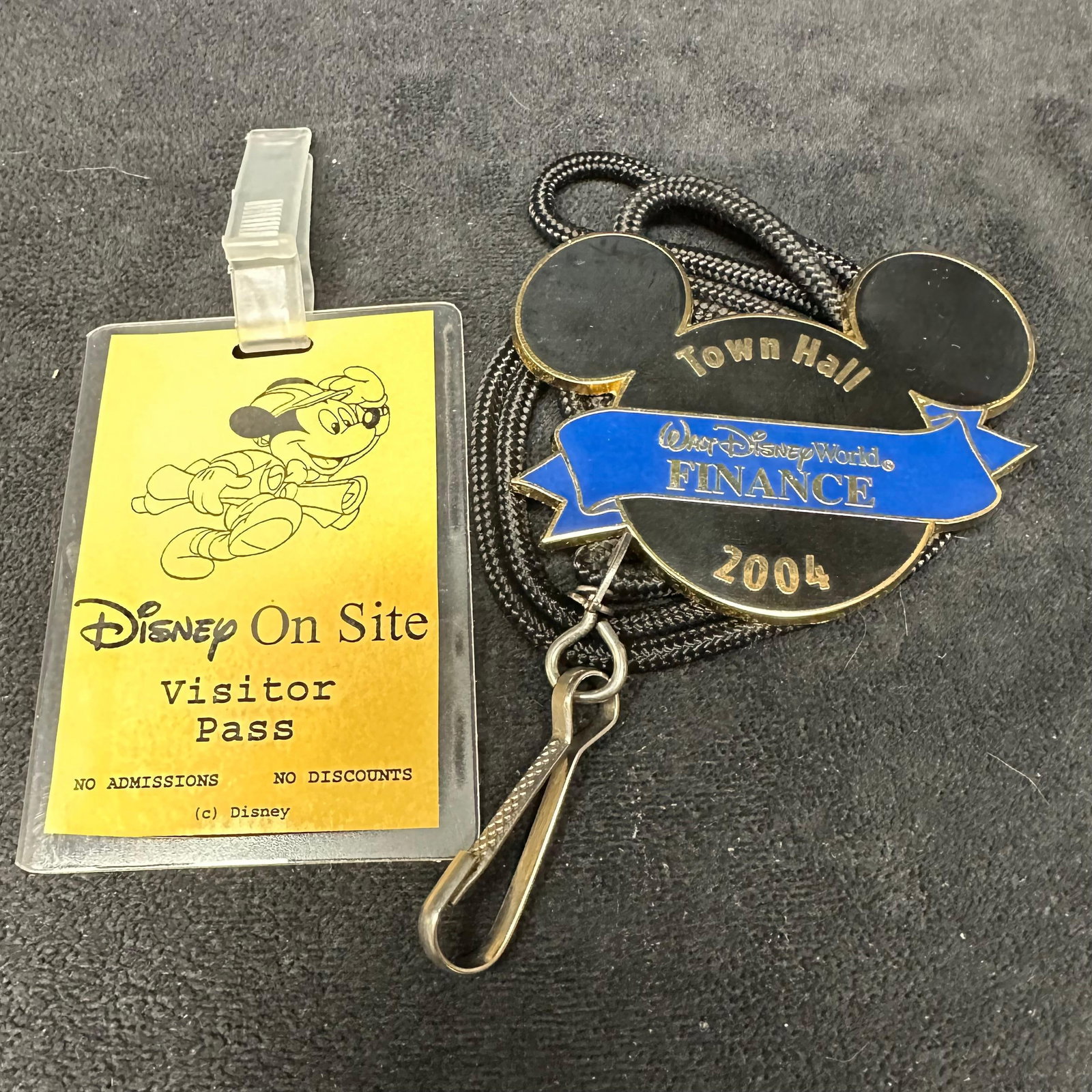 Walt Disney World Finance 2004 Town Hall Badge and Rare On Site Visitor Pass: Lot includes an official Walt Disney World Finance 2004 Town Hall badge in the shape of Mickey Mouse with blue enamel detail, attached to a black lanyard, along with a Disney On Site Visitor Pass feat