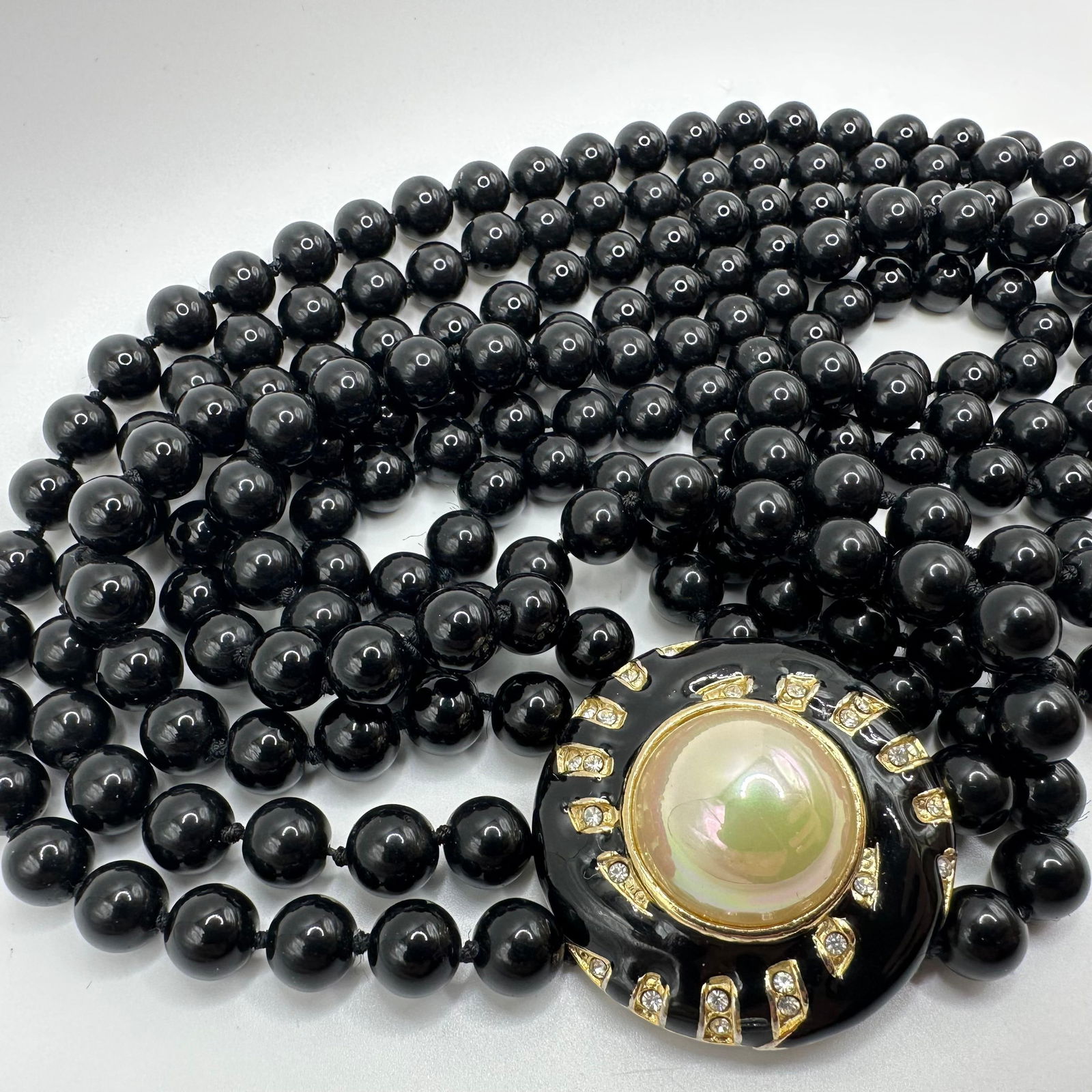 Vintage Multi Strand Black Beaded Necklace Prominent Centerpiece Faux Pearl and Rhinestones: Vintage triple-strand black bead necklace featuring a prominent centerpiece with a faux pearl surrounded by black enamel and rhinestones. No hallmarks. This item is in good pre-owned, previously used/
