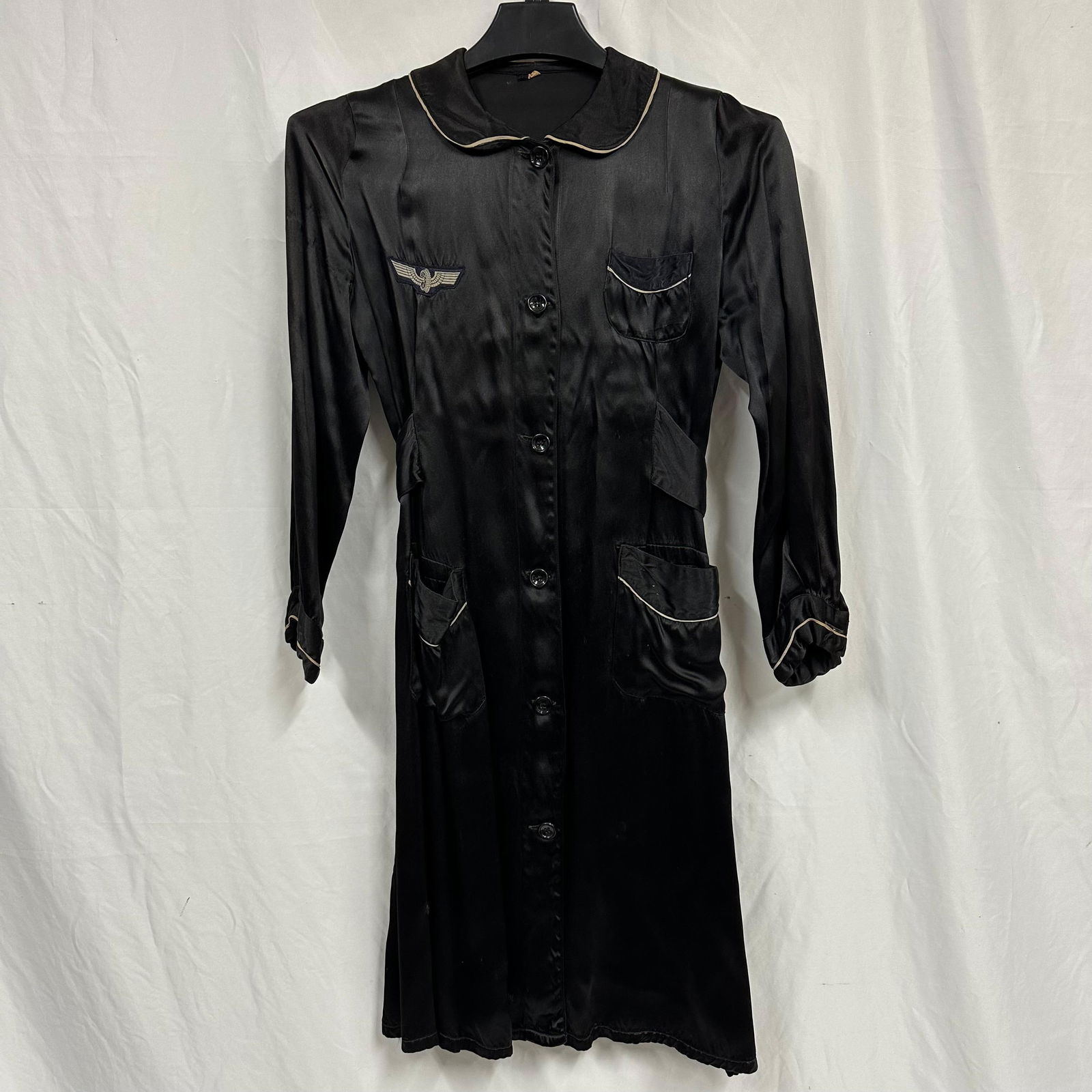 Vintage Black Satin Uniform Long Dress Shirt Coat Rob Style with Wing Insignia: Vintage black satin uniform-style long dress shirt featuring long sleeves, button-front closure, contrast piping at the collar and pockets, and multiple front pockets. Includes a winged insignia