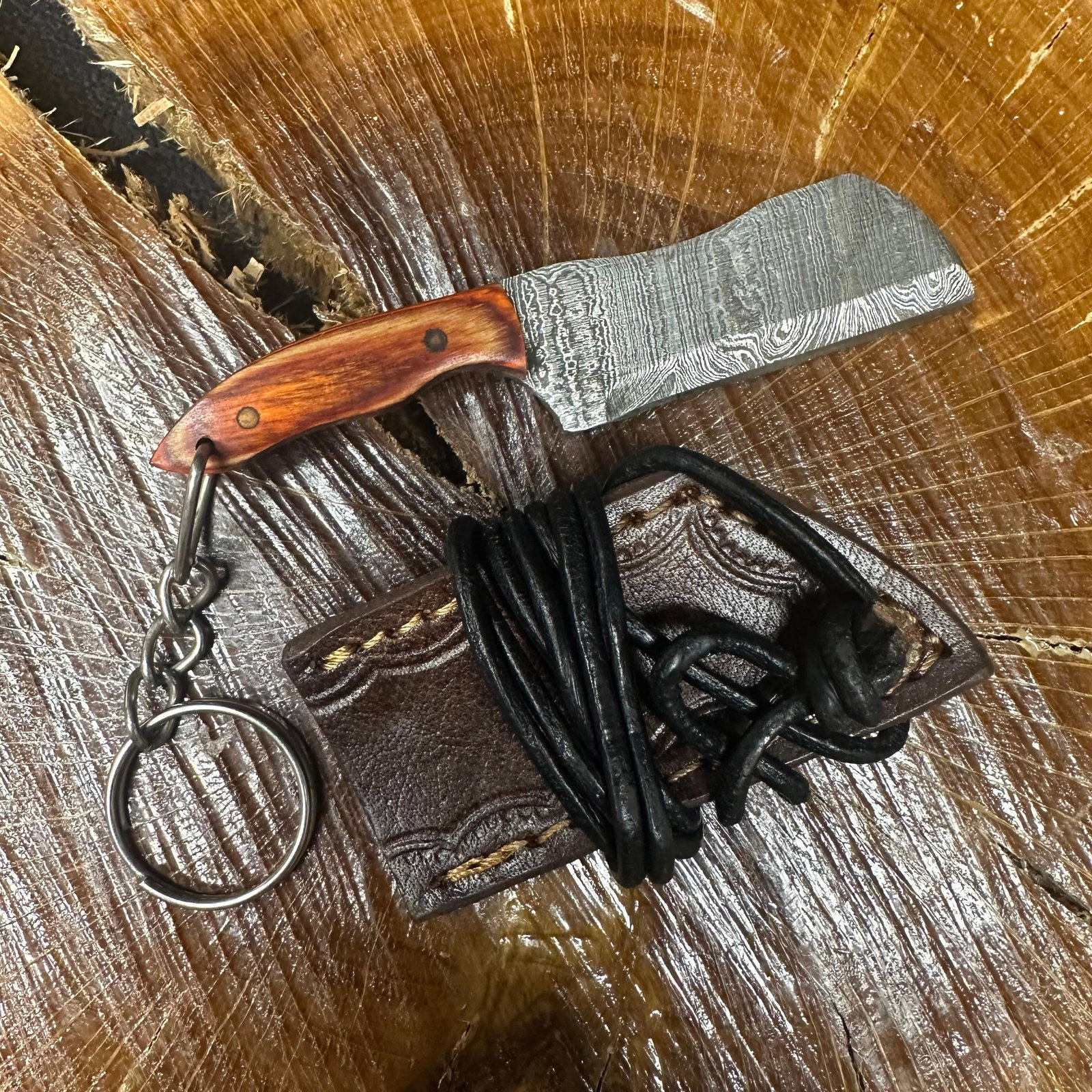 MHS Cutlery Keychain Cleaver Style Blade Knife With Leather Case Necklace R42: Small key chain-sized fixed-blade knife featuring a patterned steel blade and a compact epoxy-resin/wood brown/orange-tone handle secured with brass pins. Includes a fitted brown leather sheath with s