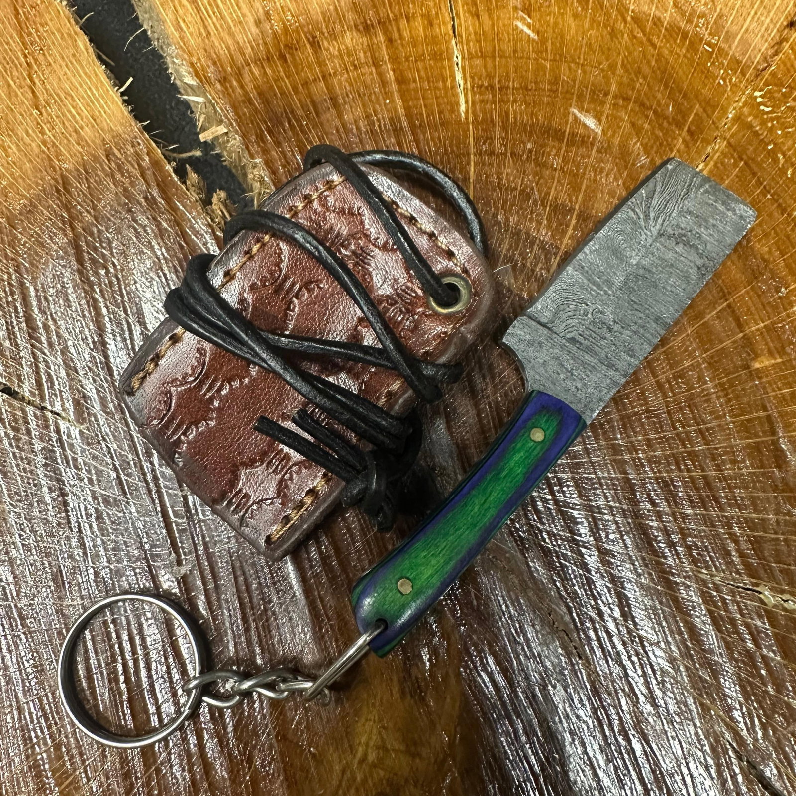MHS Cutlery Keychain Cleaver Style Blade Knife With Leather Case Necklace R40: Small key chain-sized fixed-blade knife featuring a patterned steel blade and a compact epoxy-resin/wood green/blue-tone handle secured with brass pins. Includes a fitted brown leather sheath with sti