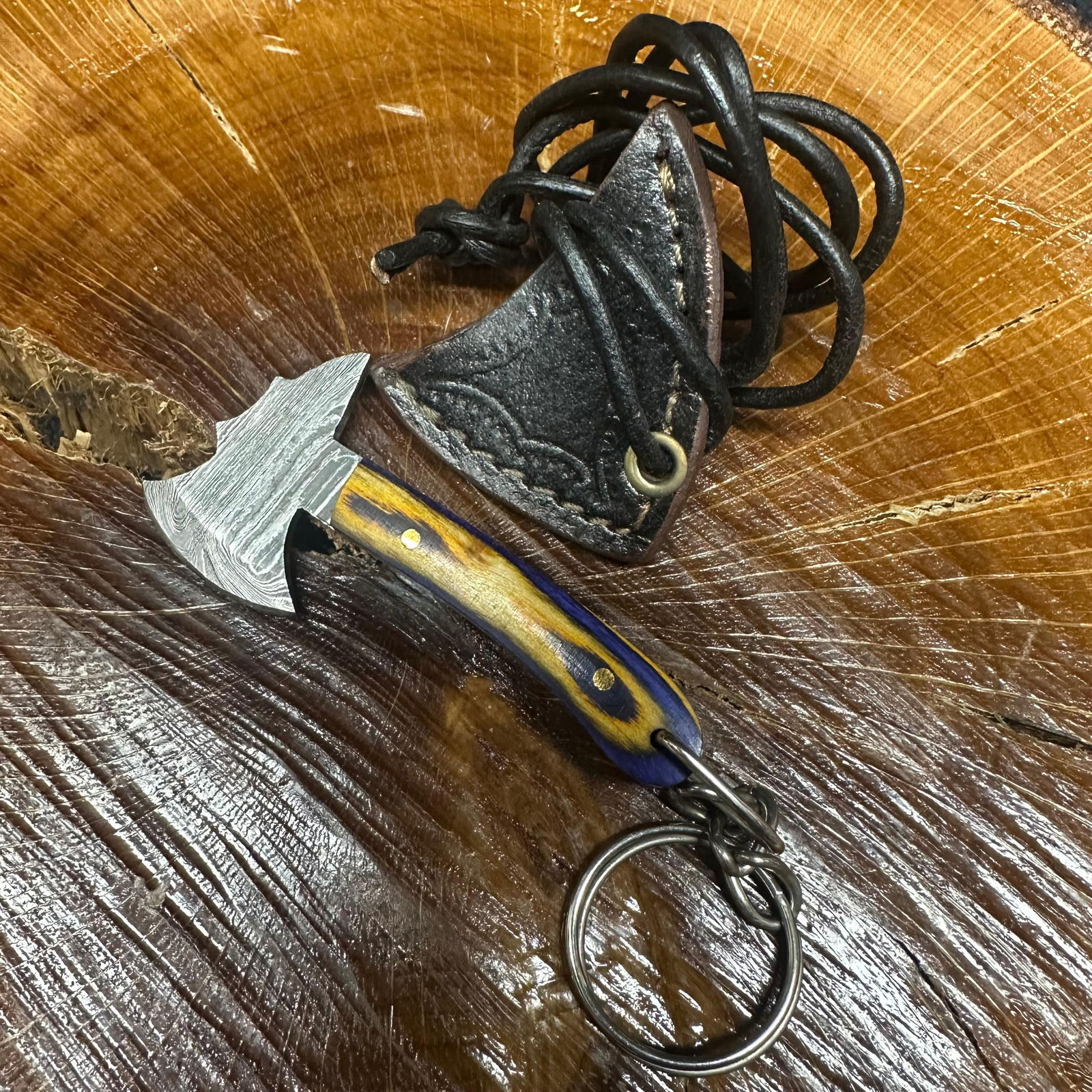 MHS Cutlery Keychain Mini Blade Axe With Leather Case Necklace R41: Small key chain-sized fixed-blade axe featuring a patterned steel blade and a compact epoxy-resin/wood tan/blue-tone handle secured with brass pins. Includes a fitted brown leather sheath with stitche