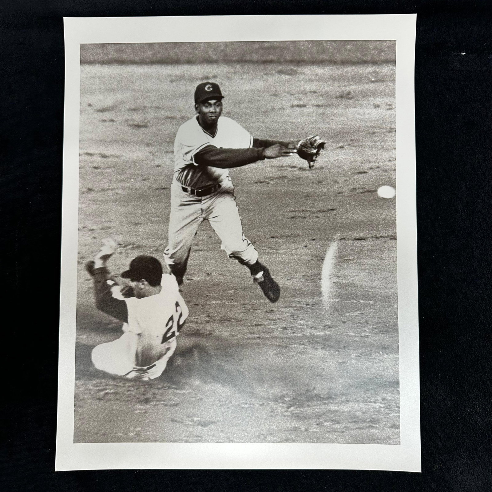 Black and White Baseball Action Analog Photo Print Infield Double Play Scene #2: Black and white analog photo print depicting an infield double play attempt. One player is captured mid-air, throwing the ball as a runner slides beneath. Blank reverse side. This item is in pre-owned