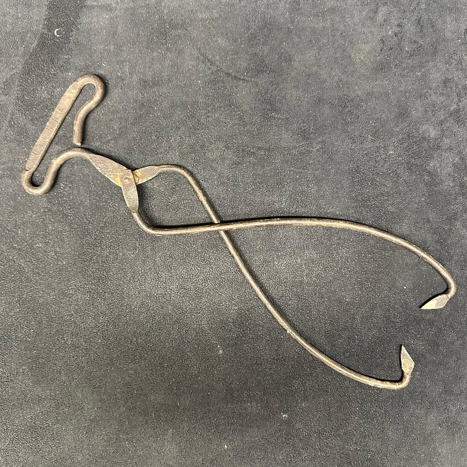 Antique Forged Iron Blacksmith Tongs with T-Handle: Antique forged iron blacksmith tongs featuring a distinctive T-shaped handle and long curved jaws. Hand-forged construction with riveted joints and pointed gripping tips, designed for holding hot meta