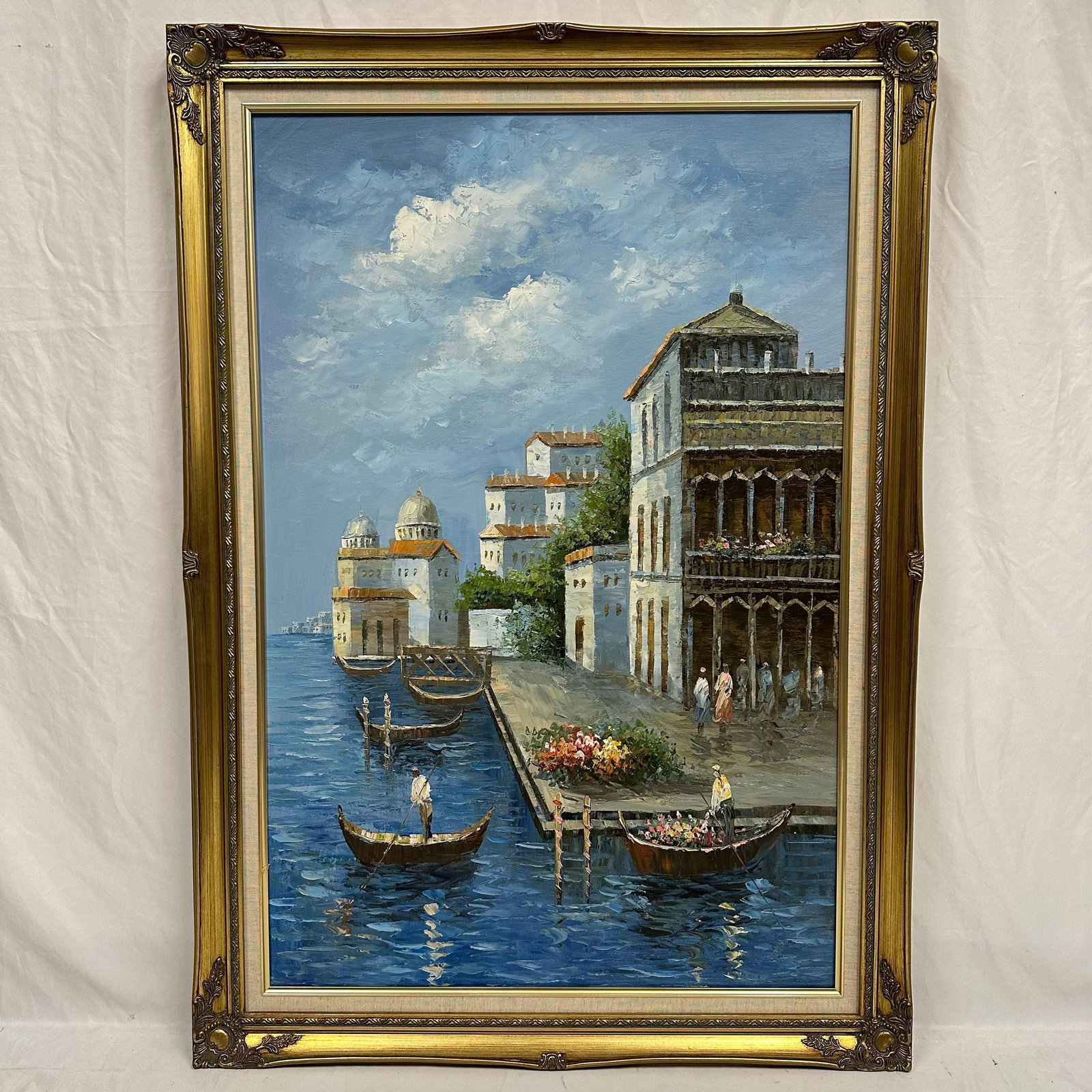 Large Venetian Canal Oil Painting Gondolas and Figures Along the Waterfront Framed: Unknown artist. Oil painting on canvas depicting a lively Venetian canal scene with gondolas drifting along the blue waters beside elegant old-world architecture. Figures walk near the flower-lined wa