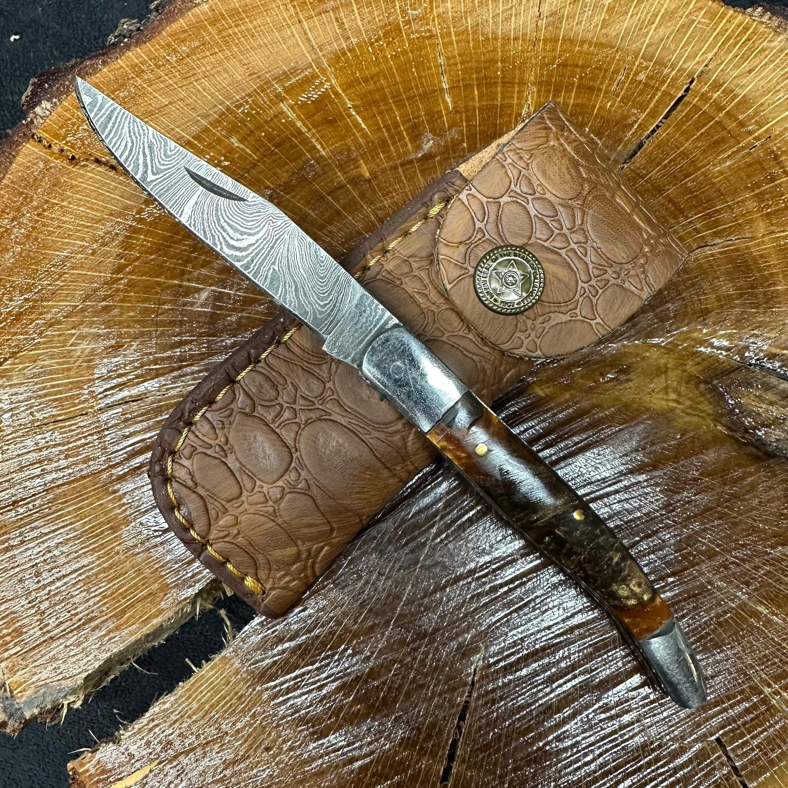 MHS Cutlery Steel Layered Patterned Folded Blade Pocket Knife Q80: Folding blade pocket knife by MHS Cutlery featuring a layered patterned steel blade and decorative spine work. The handle has a contoured, wood/resin-style grip with metal mosaic pin accents. Includes