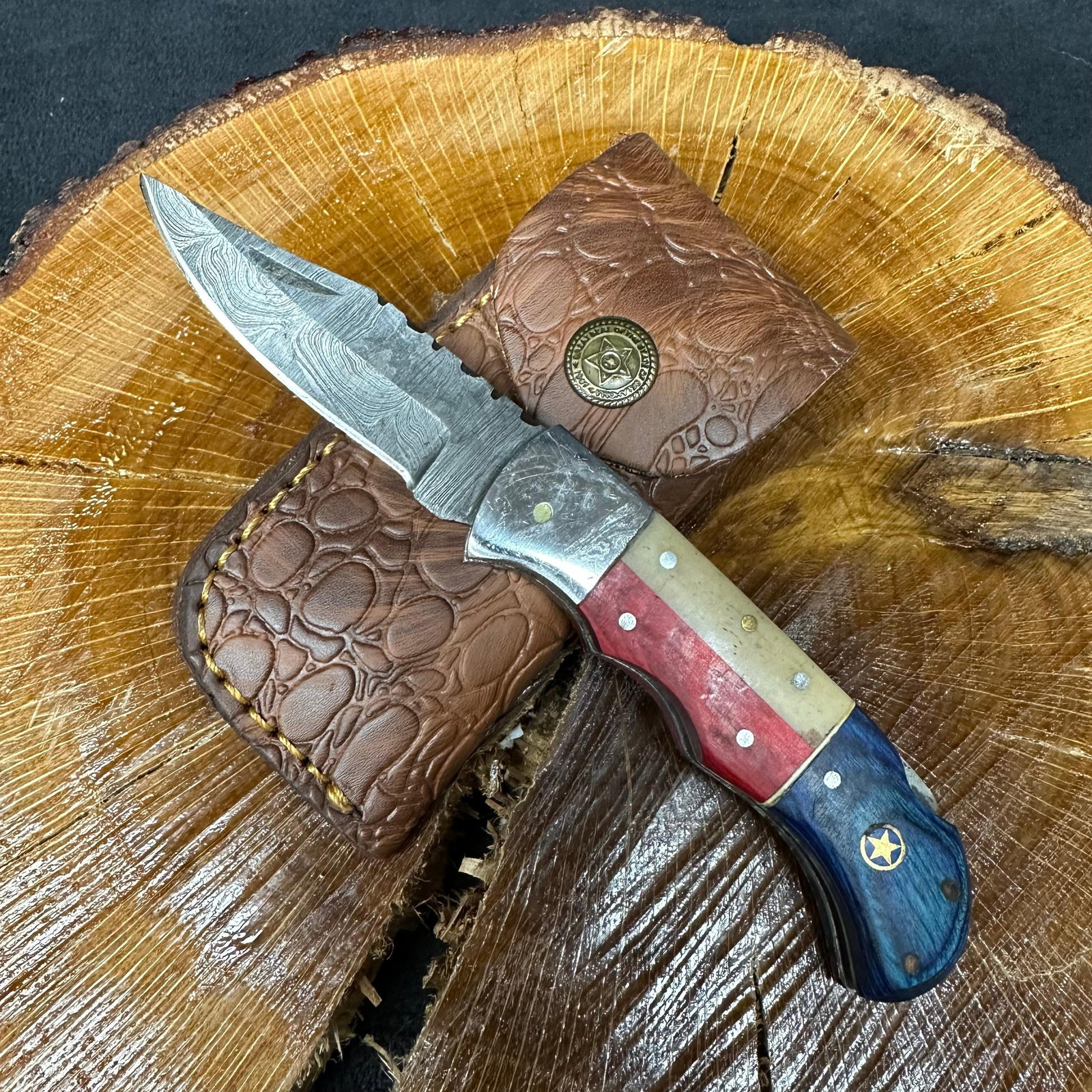 American Themed MHS Cutlery Steel Folded Blade Pocket Knife with Brown Sheath Q90: Folding blade pocket knife by MHS Cutlery featuring a layered patterned steel blade and decorative spine work. The handle has a contoured, red, white, and blue American-themed wood/resin-style grip wi