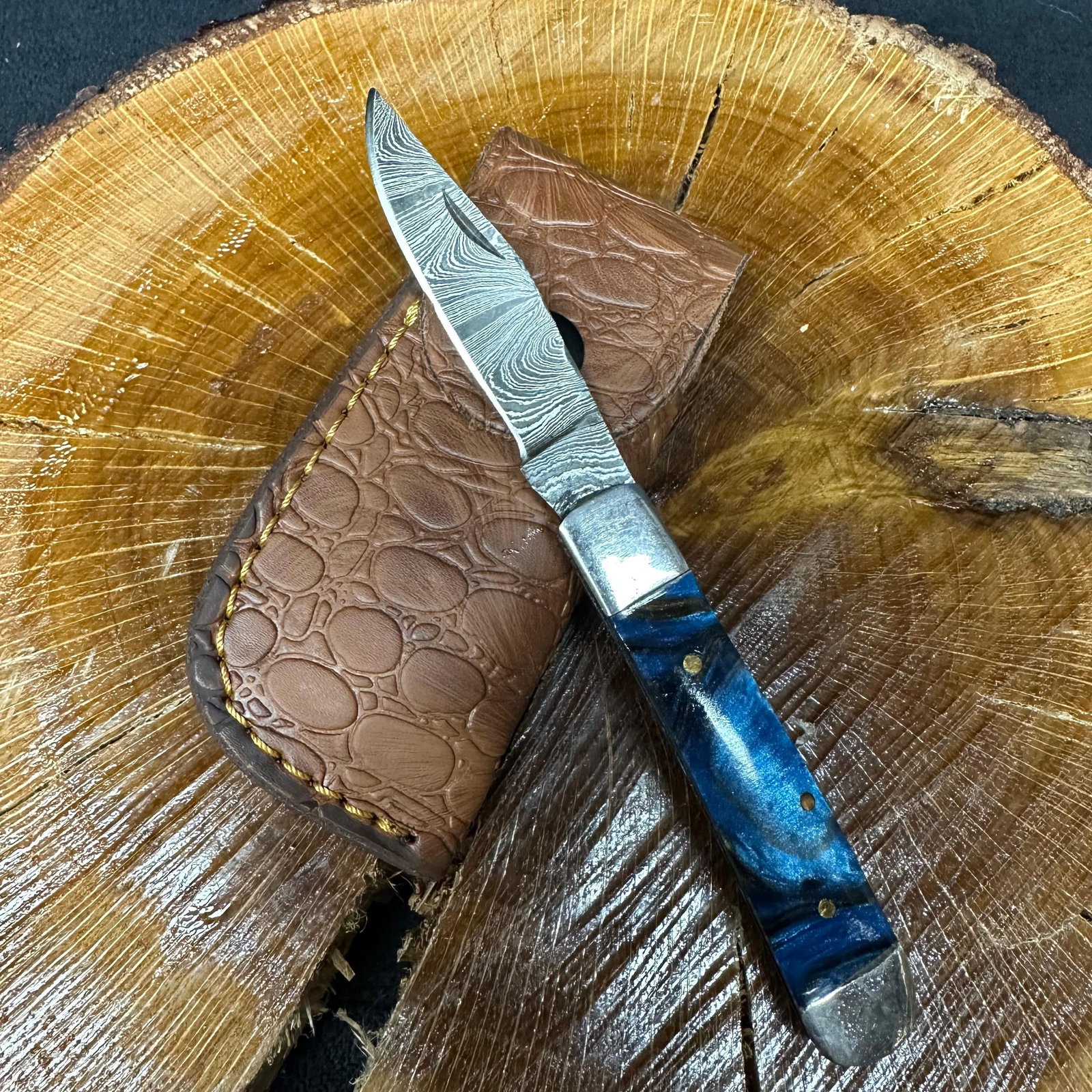 MHS Cutlery Steel Folded Blade Pocket Knife Blue Black Handle Q91: Folding blade pocket knife by MHS Cutlery featuring a steel blade and decorative spine work. The handle has a contoured, wood/resin-style grip with metal mosaic pin accents. Includes a fitted brown le