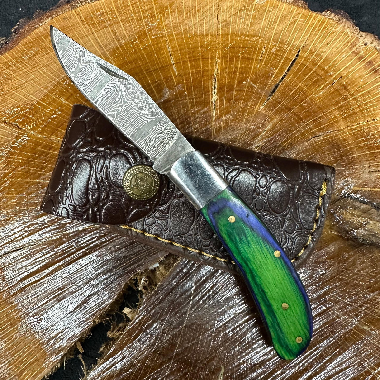 MHS Cutlery Steel Folded Blade Pocket Knife Green Blue Handle Design Q76: Folding blade pocket knife by MHS Cutlery featuring a layered patterned steel blade and decorative spine work. The handle has a contoured, green and blue colorway wood/resin-style grip with metal mosa