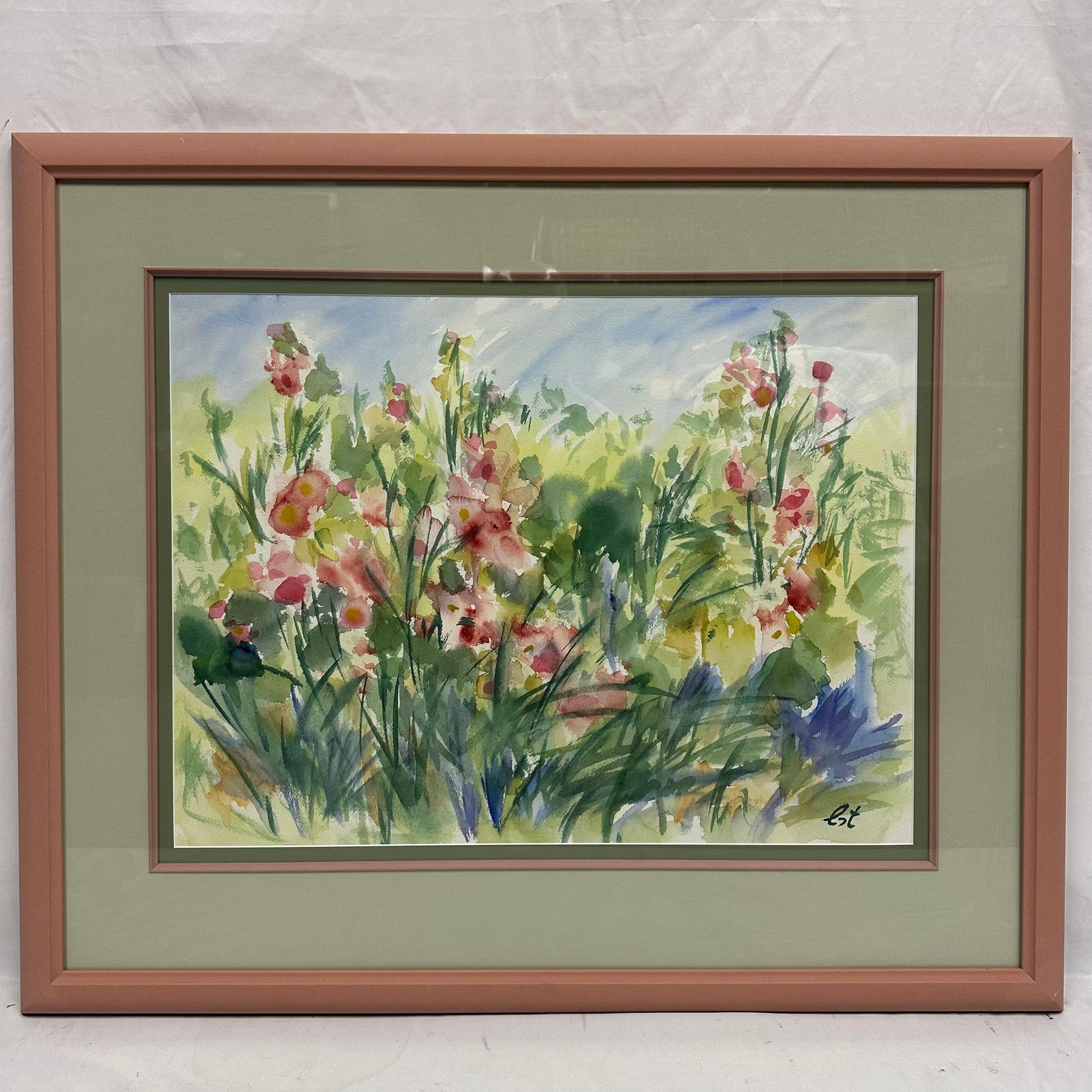 Framed Watercolor Floral Garden Scene Signed Est Pink Frame: Framed watercolor painting depicting a vibrant garden scene with pink wildflowers and lush green foliage. Signed, Est, at the lower right. Housed in a double-matted pink frame with glass. Artwork