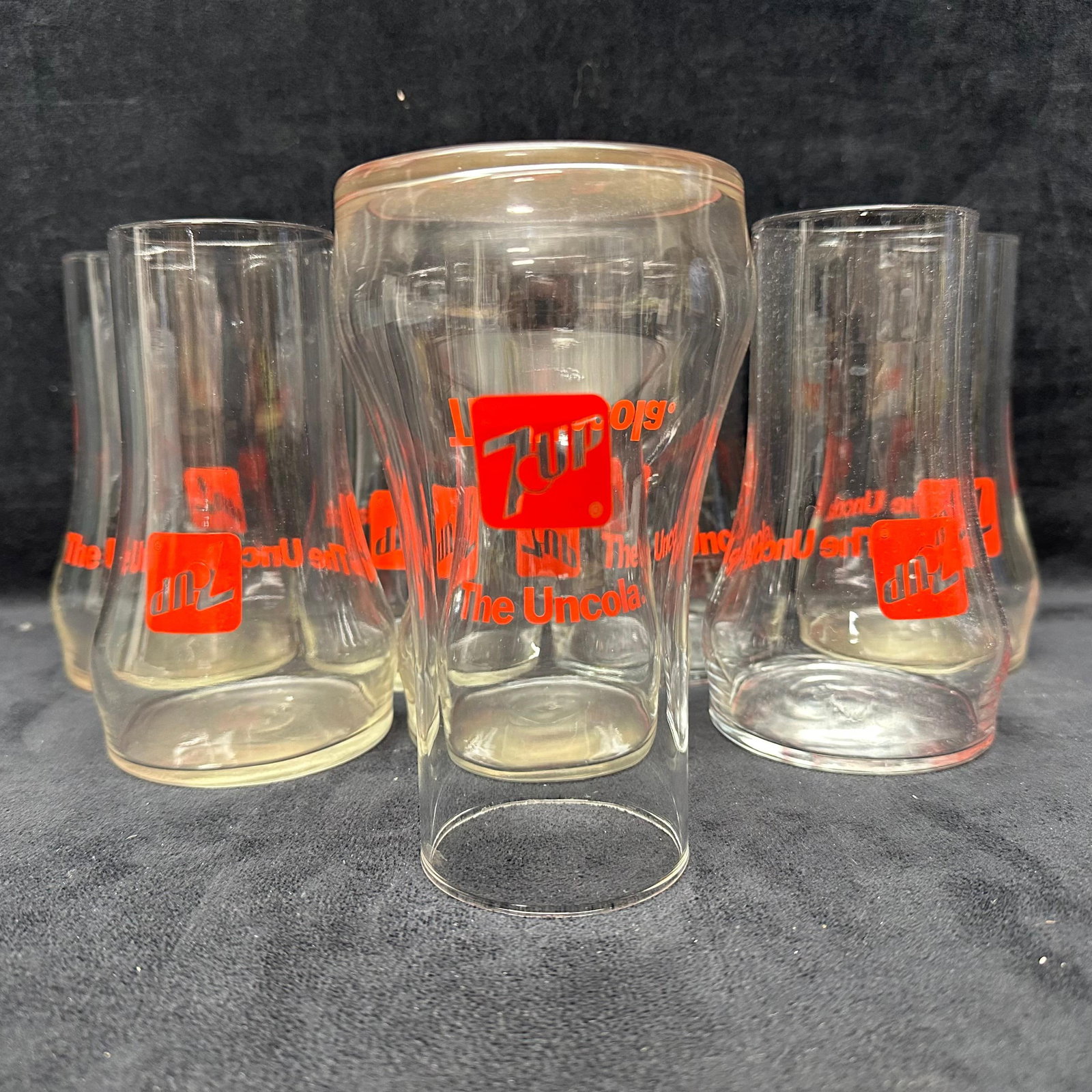 Set of 8 Vintage 7UP The Uncola Drinking Glasses: Group of eight vintage 7UP advertising glasses featuring red “7UP” logo and The Uncola slogan. Includes a mix of flared and straight-sided forms. Clear glass construction. Light wear, some haz