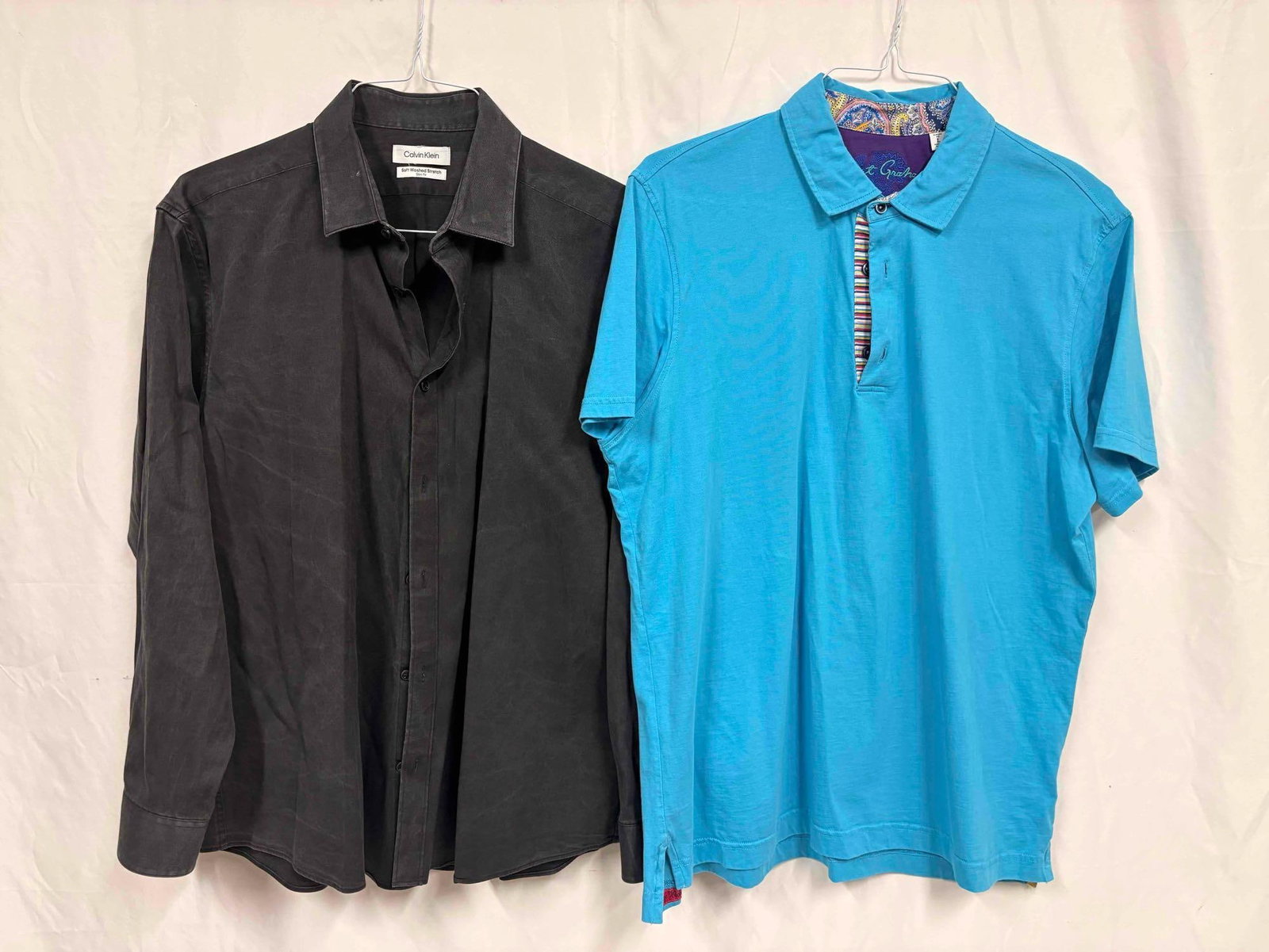 2PC Calvin Klein and Robert Graham Casual Blue and Dark Grey Mens Shirt Bundle: This lot contains a set of men's short sleeve dress shirts. Both the Robert Graham and Calvin Klein shirts stand in like-new conditions without tags. Please refer to images for further context on