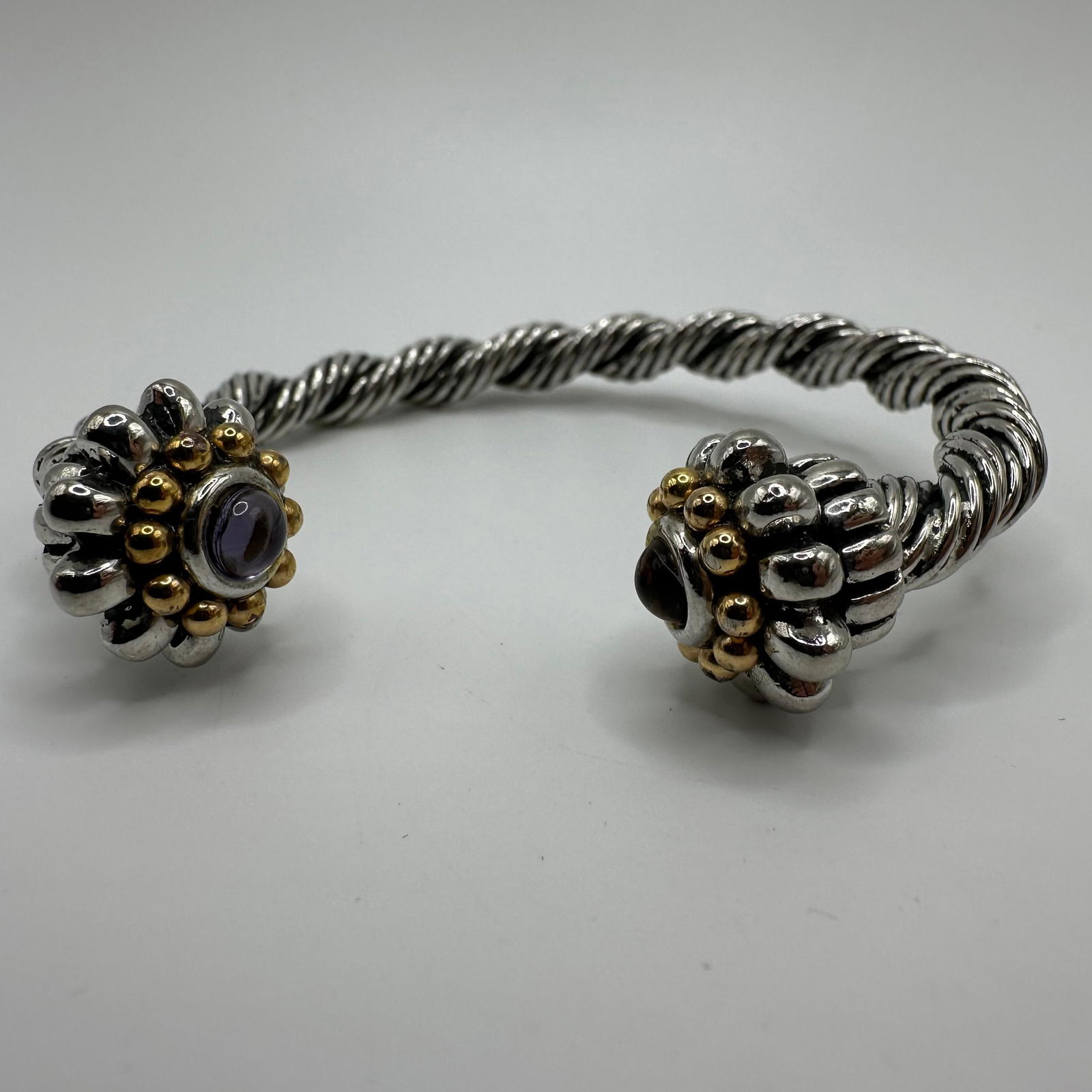 Twisted Cable Design Silver and Gold Tone Purple Glass Accent Cuff Bracelet: No hallmarks. Silver and gold-toned base metal with purple glass accents. This item is in good pre-owned, previously displayed condition with light wear and surface markings. Please reference all phot