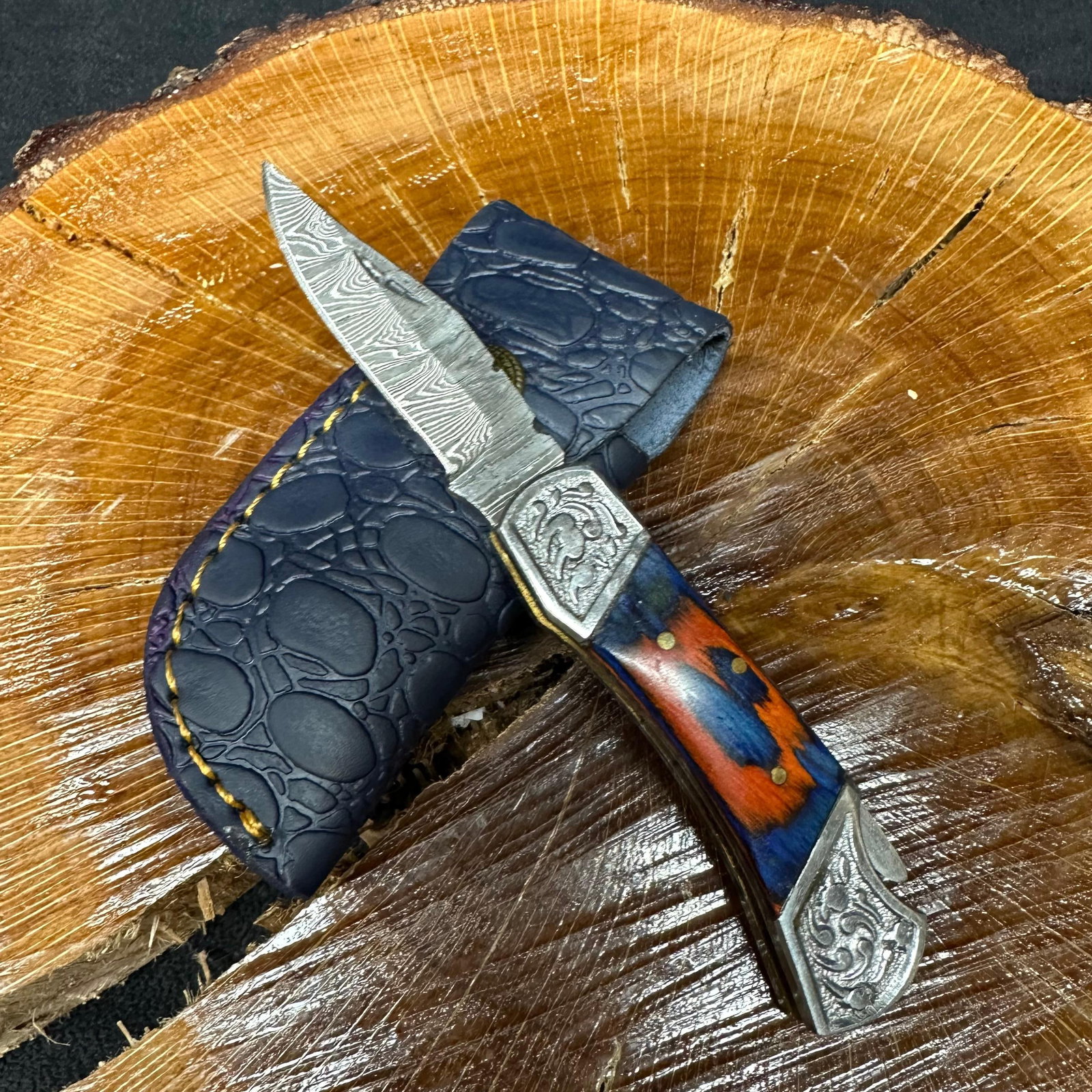 MHS Cutlery Steel Folded Blade Pocket Knife Orange and Blue Handle Q83: Folding blade pocket knife by MHS Cutlery featuring a layered patterned steel blade and decorative spine work. The handle has a contoured, blue-and-orange wood/resin-style grip with metal mosaic pin a