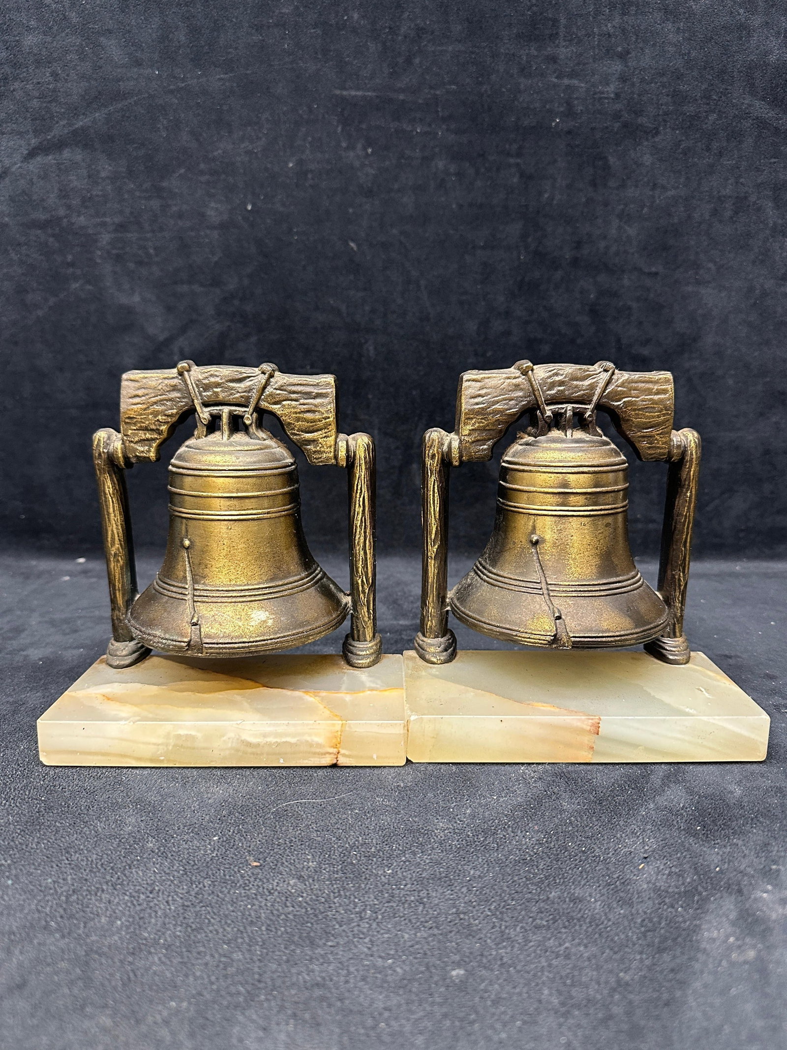 Pair Bronze Tone Liberty Bell Bookends Onyx Bases: Pair of bronze-tone Liberty Bell form bookends with sculpted wood supports mounted on polished onyx or marble bases. Felted undersides with maker labels present. Light wear from age and use. 1974 SCC 