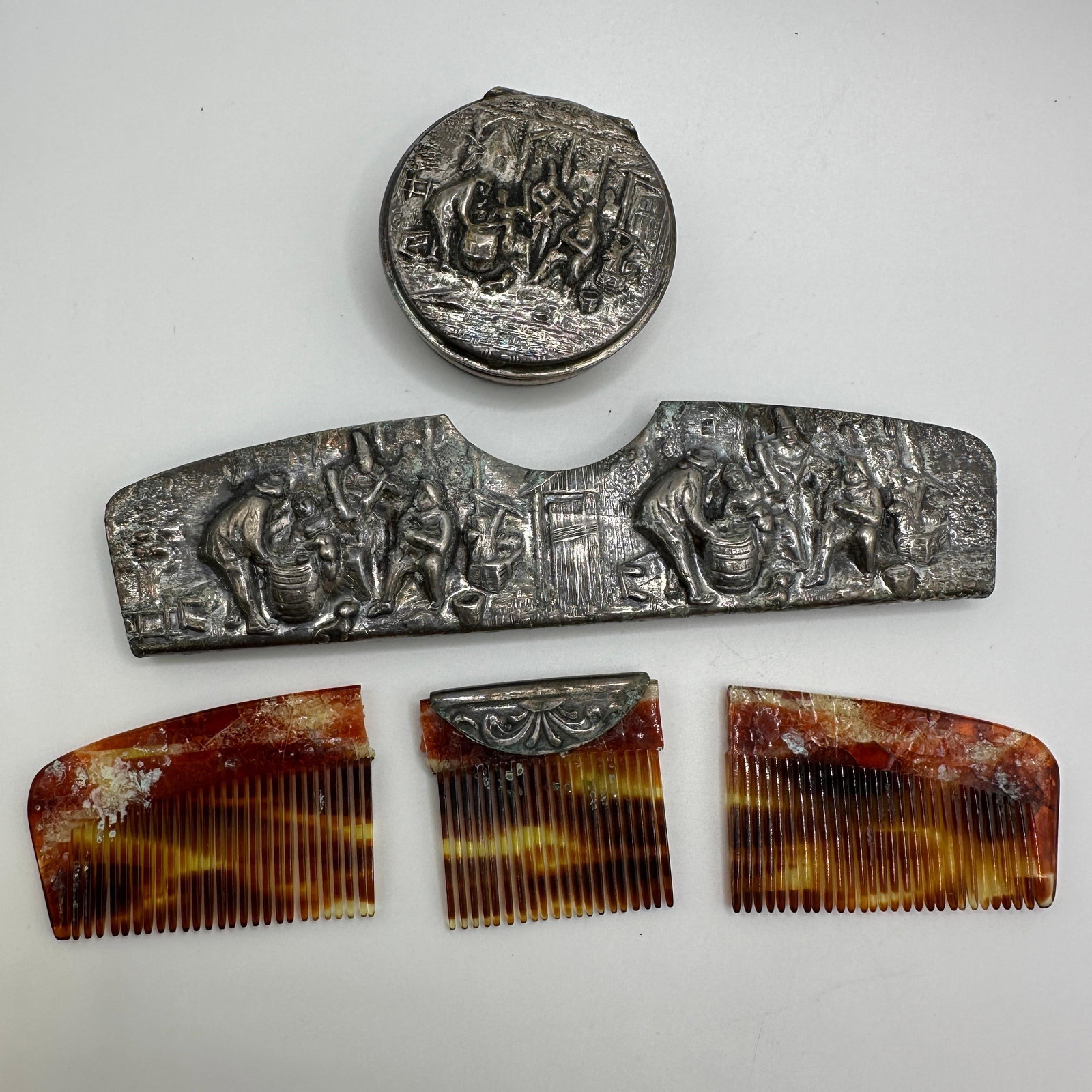 Danish Silver Plated Vanity Set With Figural Relief And Faux Tortoiseshell Comb: Group of vintage Danish silver-plated vanity items, including a round lidded box, a figural relief comb handle or frame with genre scenes, and a broken faux tortoiseshell style comb, one piece with a 