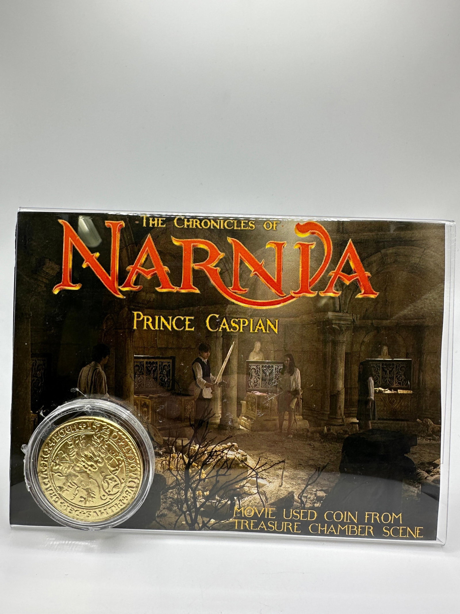 Chronicles Of Narnia Prince Caspian Movie Used Treasure Chamber Coin: Promotional display featuring a metal coin used in the production of The Chronicles of Narnia: Prince Caspian, presented in original display card and plastic holder. Coin is accompanied by a Certifica