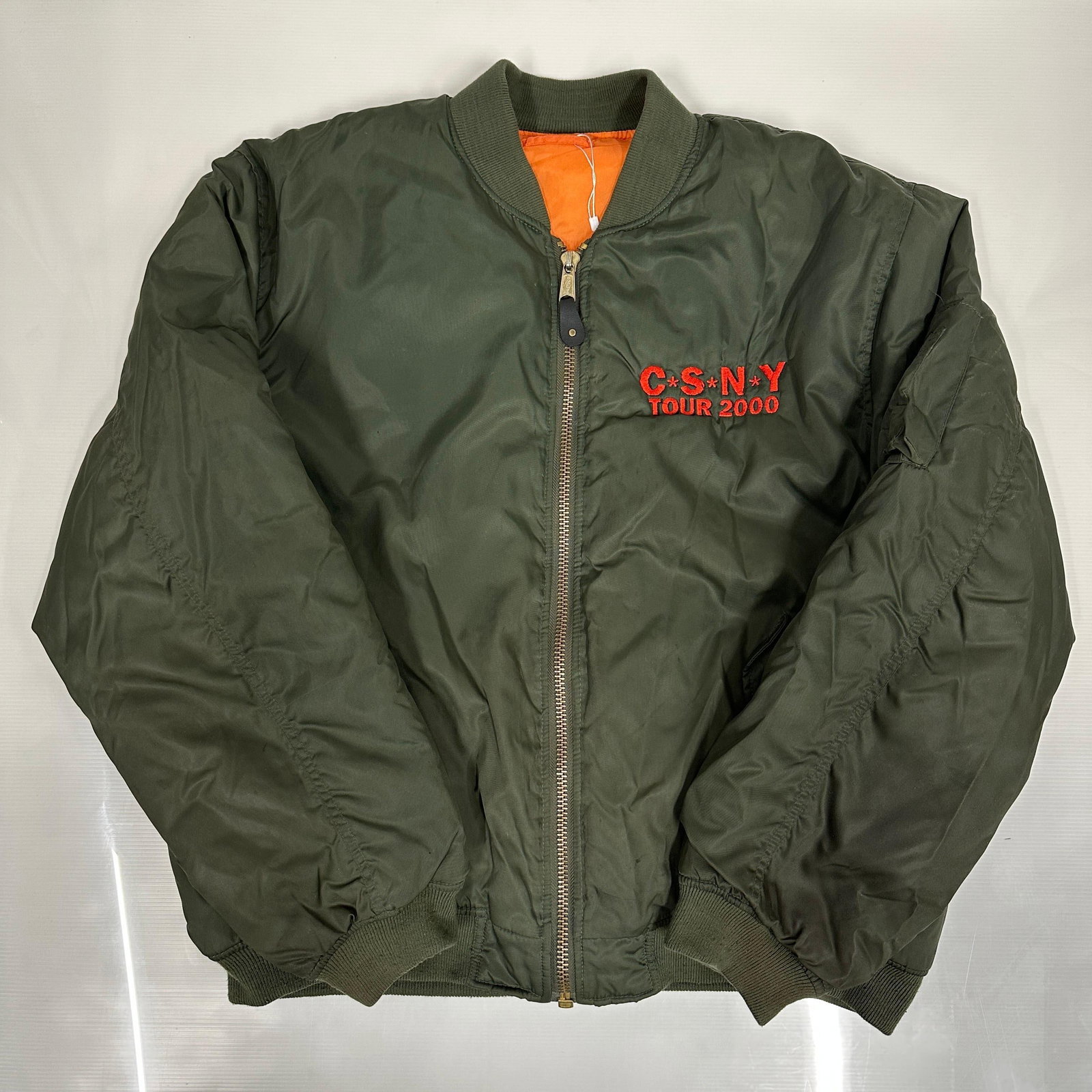 Crosby Stills Nash and Young CSNY Tour 2000 Bomber Jacket Green Orange: Vintage Crosby, Stills, Nash, and Young (CSNY) Tour 2000 reversible MA-1 style bomber jacket in olive green with orange interior lining. Embroidered red CSNY Tour 2000 logo at chest with front zip clo