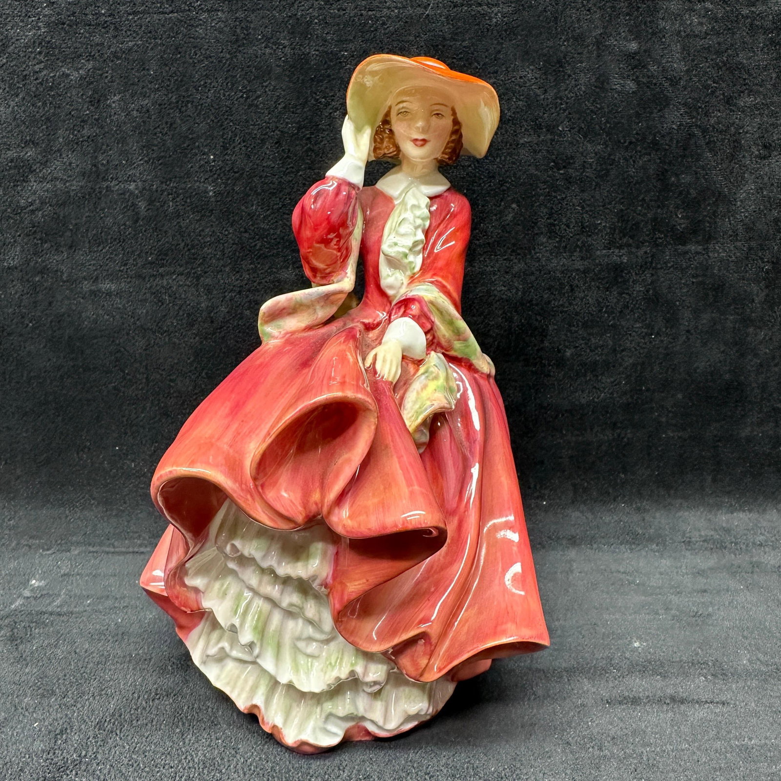 Royal Doulton Top O The Hill HN 1834 Bone China Figurine: Royal Doulton English bone china figurine titled Top O The Hill, model HN 1834. Depicts a seated lady in a flowing red and pink dress with a wide-brimmed hat. Green Royal Doulton backstamp to undersid