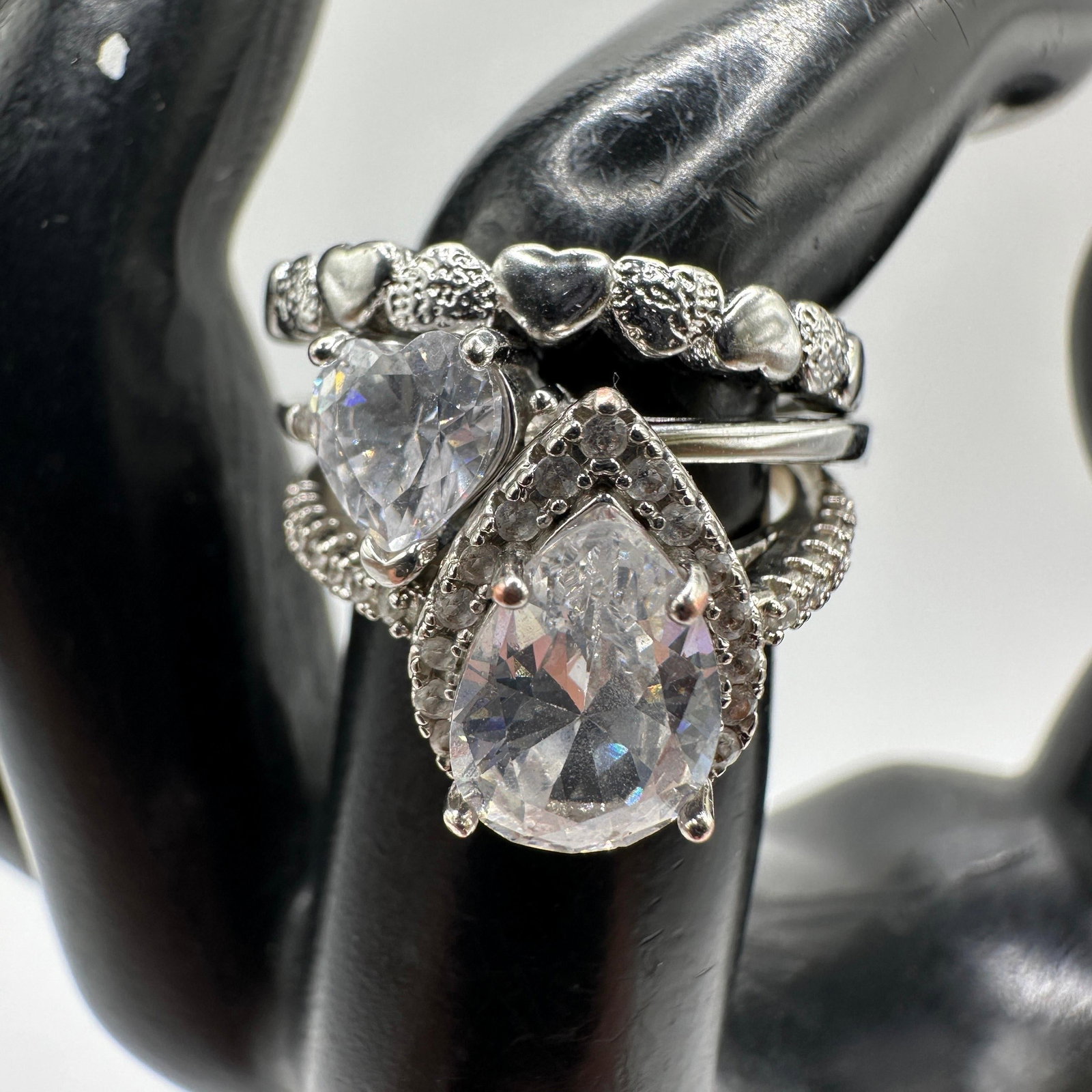 Marked Costume Jewelry Ring Group CZ Accents: Group of four silver-tone fashion rings marked “925,” including heart motif, pear shape, and heart cut simulated stone examples with rhinestone/cubic zirconia accents. All rings tested neg