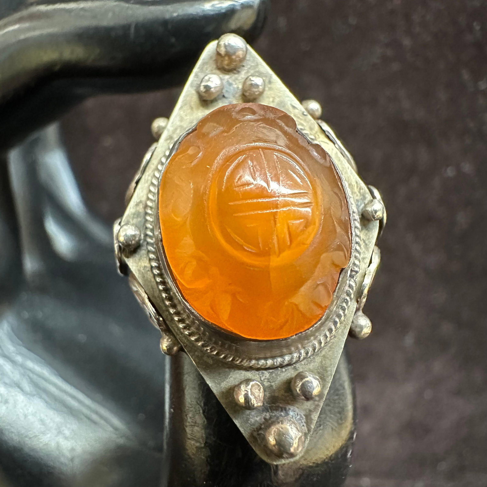Carved Orange Glass Cabochon Silver Plated Ring: Vintage silver-plated statement ring featuring a carved orange glass cabochon with decorative engraved details. The ring showcases a raised bezel and ornate metalwork with leaf and bead accents. This 