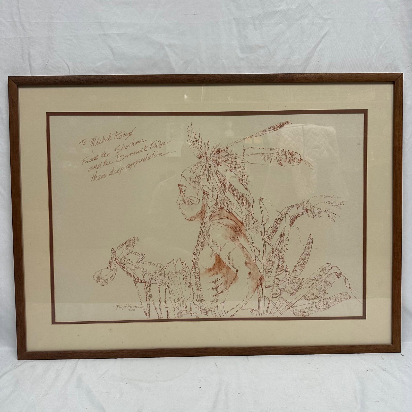 Ralph Harris Shoshone and Bannock Warrior Signed Artwork with Dedication: Framed artwork by artist Ralph Harris, depicting a Native American warrior in detailed line work with a feathered headdress and traditional regalia. The piece includes a handwritten dedication: “