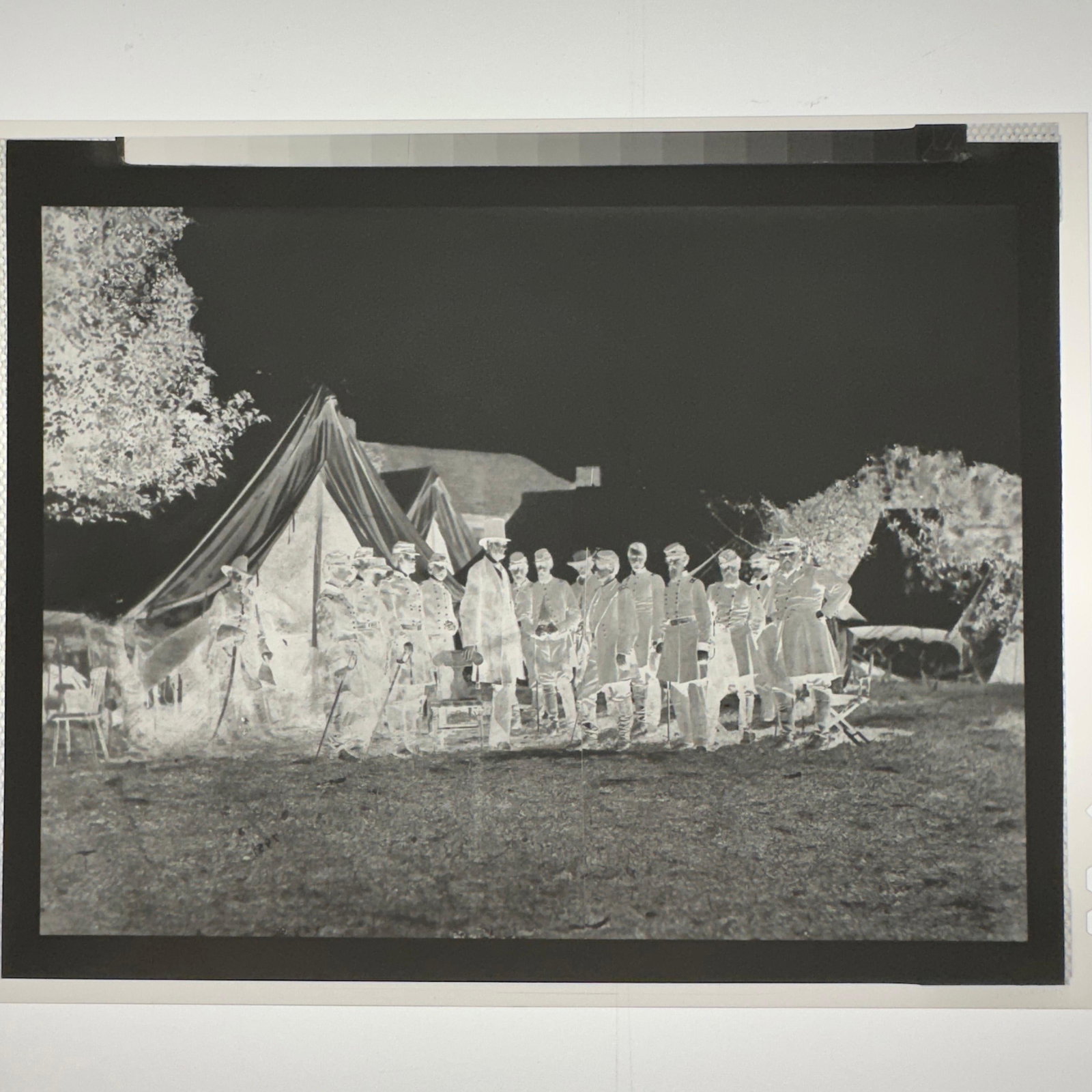 Lincoln at McCellan Headquarters Civil War Scene Photographic Archival Negative: Small black and white photographic archival negative depicting a Civil War-style historical encampment scene with uniformed figures standing outside military tents. Includes original glassine storage