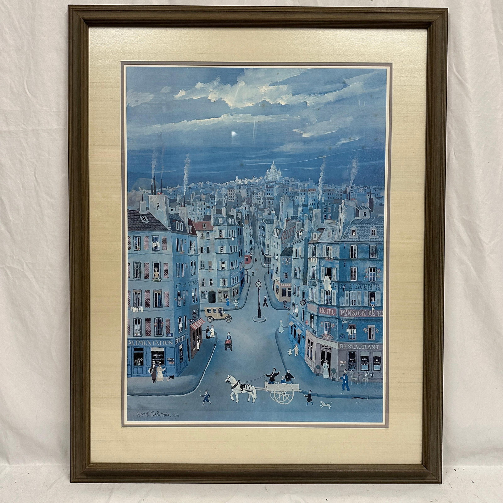 Michel Delacroix Paris Street Scene Framed Print Montmartre Titled: Framed print after Michel Delacroix depicting a Parisian street scene with figures, a horse cart, storefronts, and a cityscape in a blue tonal palette. Print Signed in plate lower left “Michel