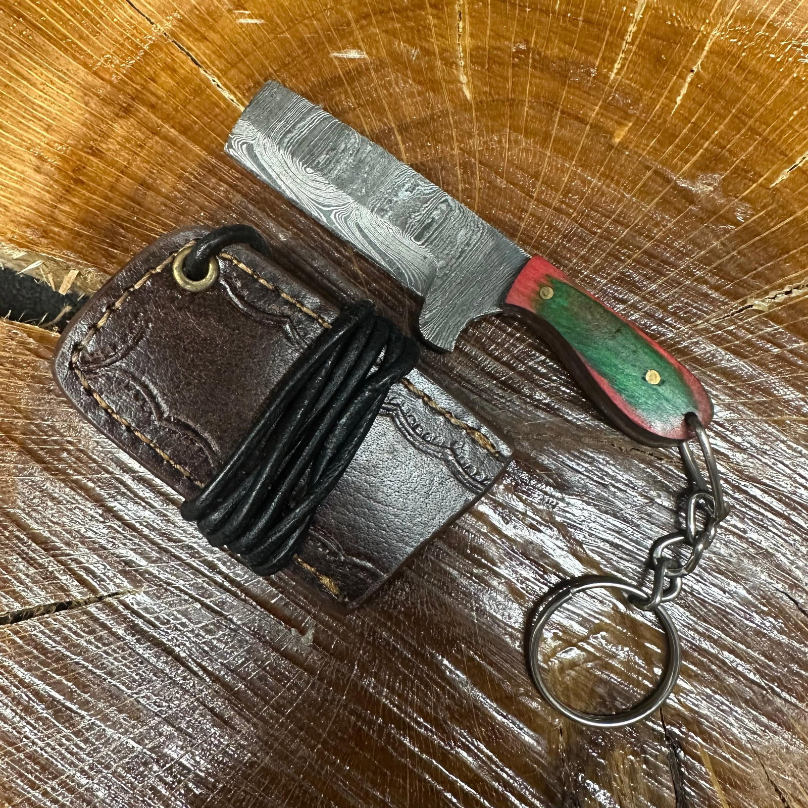 MHS Cutlery Keychain Cleaver Style Straight Blade Knife With Leather Case Necklace R43: Small key chain-sized fixed-blade knife featuring a patterned steel blade and a compact epoxy-resin/wood green/red-tone handle secured with brass pins. Includes a fitted brown leather sheath with stit
