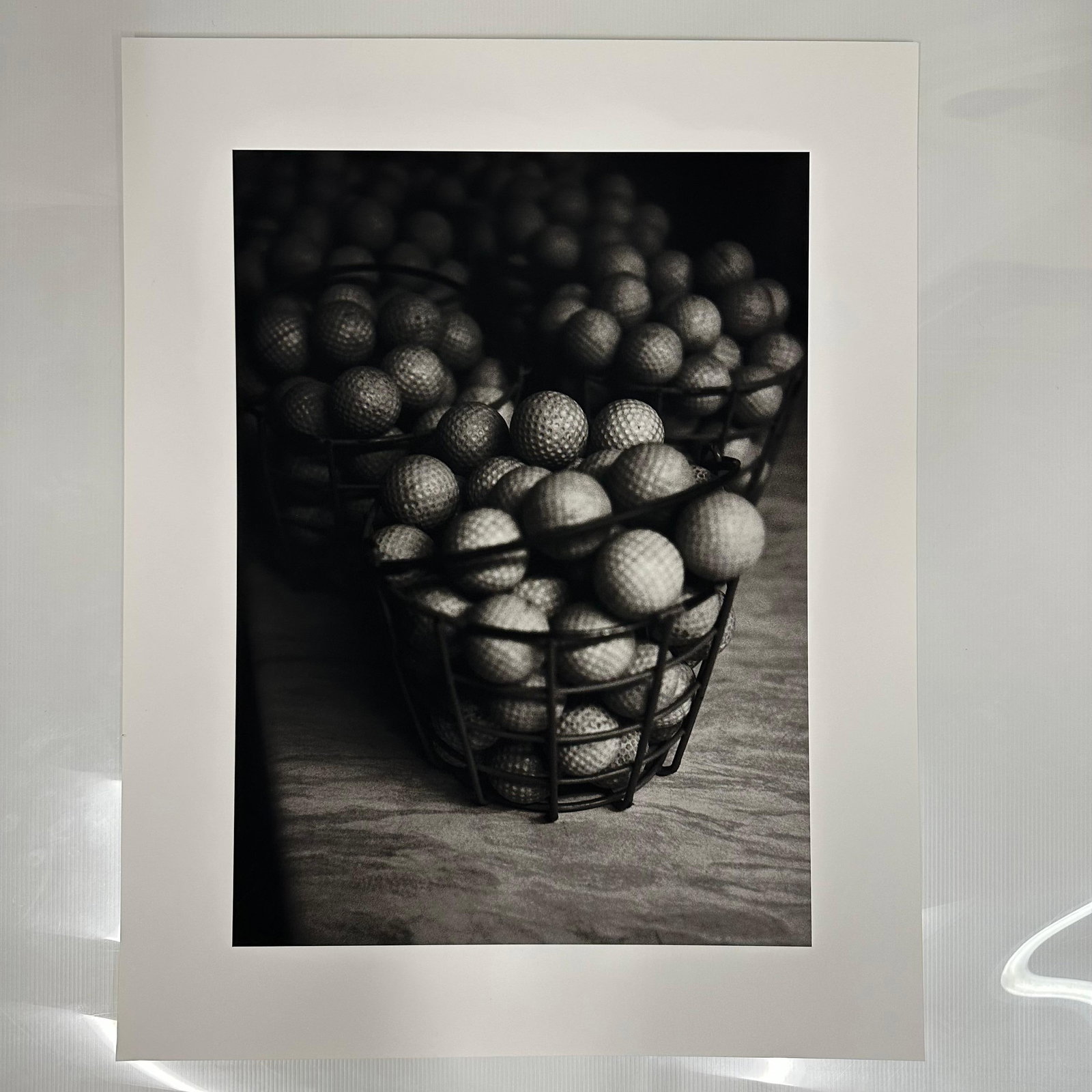 Michael Faye Buckets of Golf Balls Black and White Photograph Fine Art Print: Black and white photograph print by Michael Faye, capturing a close-up still life of golf balls stacked in wire baskets. Printed on high-quality archival matte photo paper with a clean white border. T