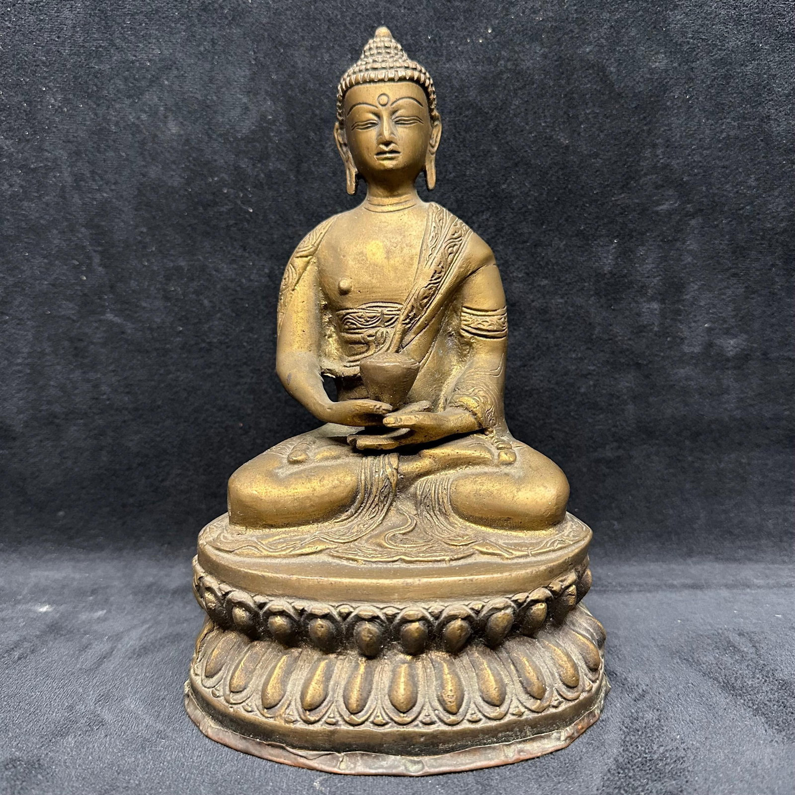 Cast Metal Seated Buddha Figure on Lotus Base Nepali or Chinese Style: Cast metal seated Buddha figure depicted in a meditative pose, holding an alms bowl, and seated on a raised lotus-form base. The figure shows detailed modeling of the facial features, robe, hair, and 