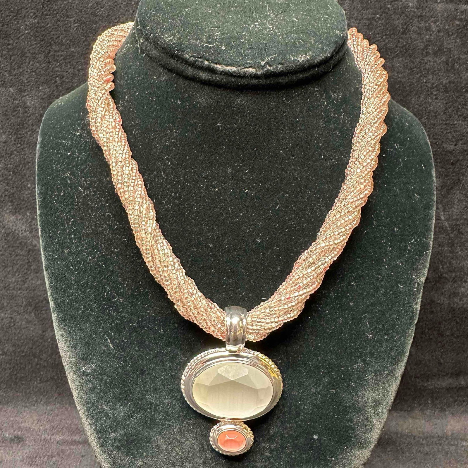 Twisted Pink Beaded Necklace with Faceted Glass and Coral-Tone Double Pendant: This elegant twisted pink seed bead necklace featuring a bold double-drop pendant. The top pendant showcases a large faceted clear glass center framed in silver-tone metal, accented below with a small