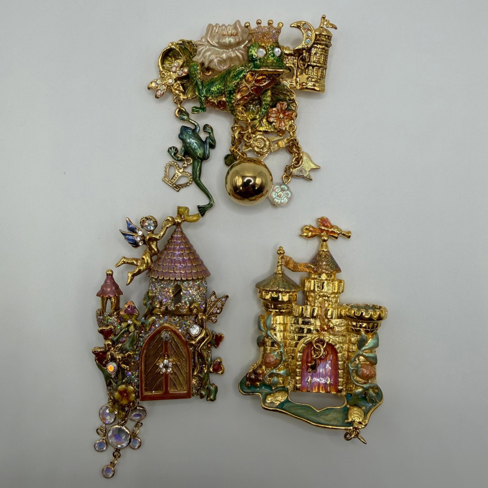 Kirks Folly Enamel Fairy Tale and Prince Frog Castle Theme Brooch Lot Three Pcs: Lot of three Kirks Folly gold-tone brooches featuring fairy tale and fantasy designs, including a crowned Prince frog, fairy cottage, and castle. Decorated with enamel, rhinestones, and dangling accen