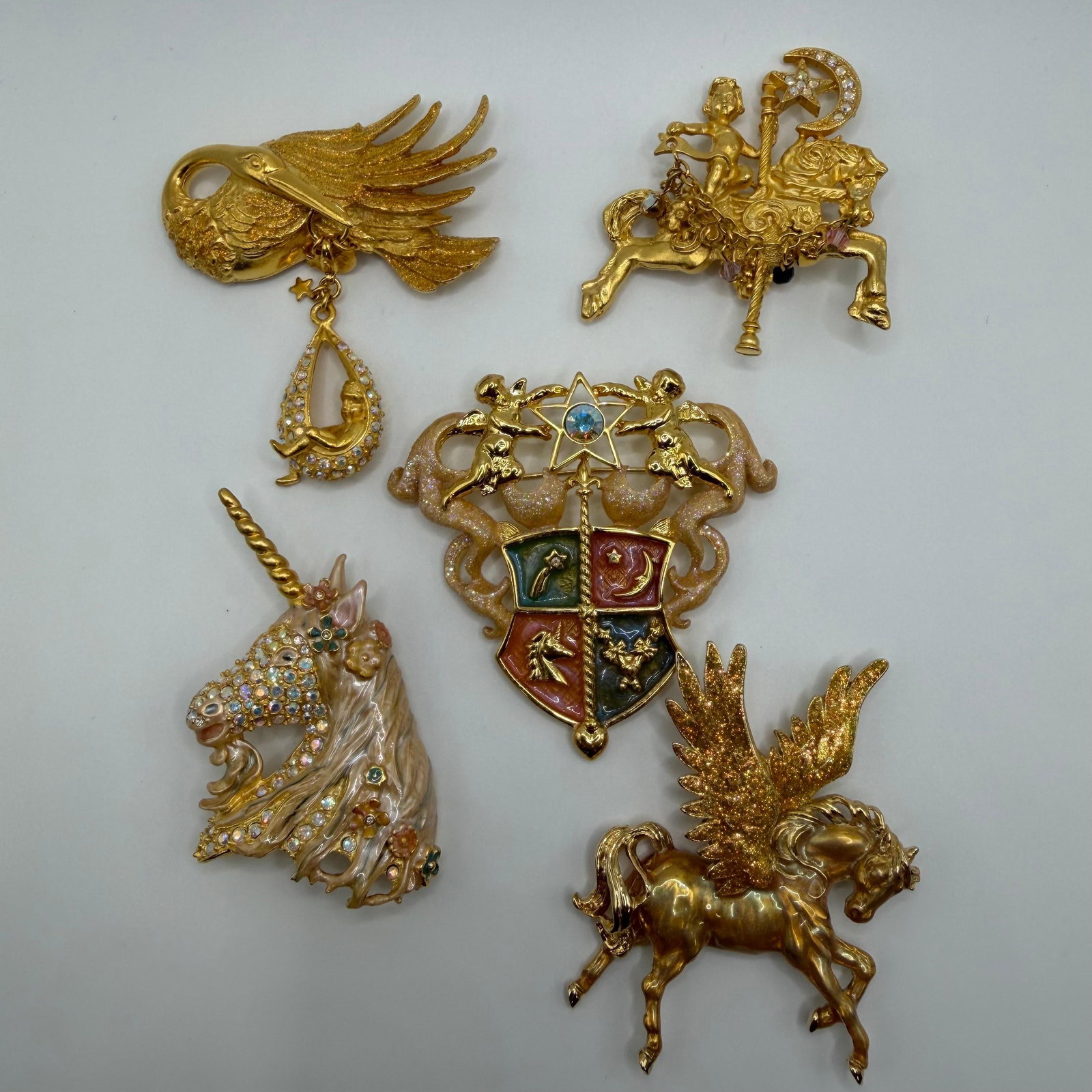 Kirks Folly Gold Tone Fantasy and Mythical Creature Horse Unicorn Brooch Lot of 5: Lot of five Kirks Folly gold-tone brooches featuring fantasy and mythical designs, including a stork, carousel horse, unicorn, heraldic crest, and Pegasus. Decorated with enamel, rhinestones, glitter 