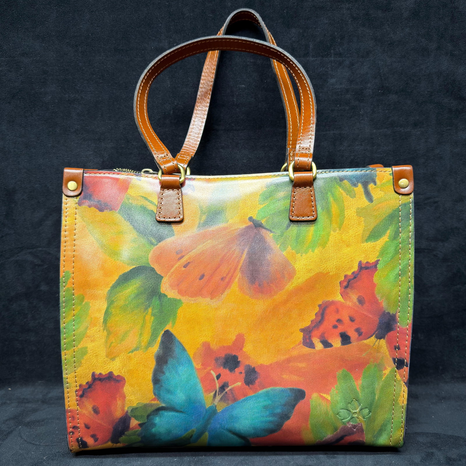 Patricia Nash Butterfly Print Leather Tote with Removable Crossbody Strap: Patricia Nash genuine leather tote featuring a vibrant butterfly and floral print exterior with cognac leather handles, zip-top closure, brass-tone hardware, and removable adjustable shoulder strap. S