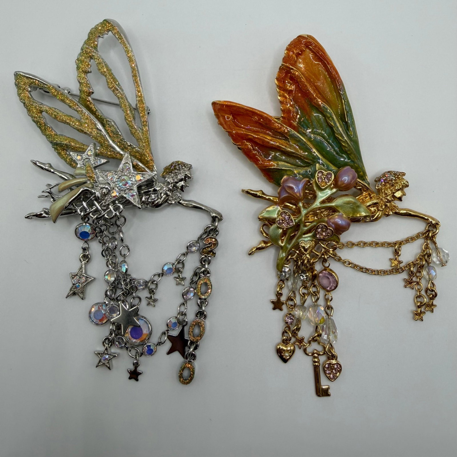 Pair of Kirks Folly Fairy Brooches with Enamel Wings and Multi Crystal Charm Dangles: Pair of fairy-themed Kirks Folly fairy brooches featuring hand-painted enamel wings and cascading charm drops. Includes one silver-tone example with glitter wings, stars, and aurora borealis crystal a