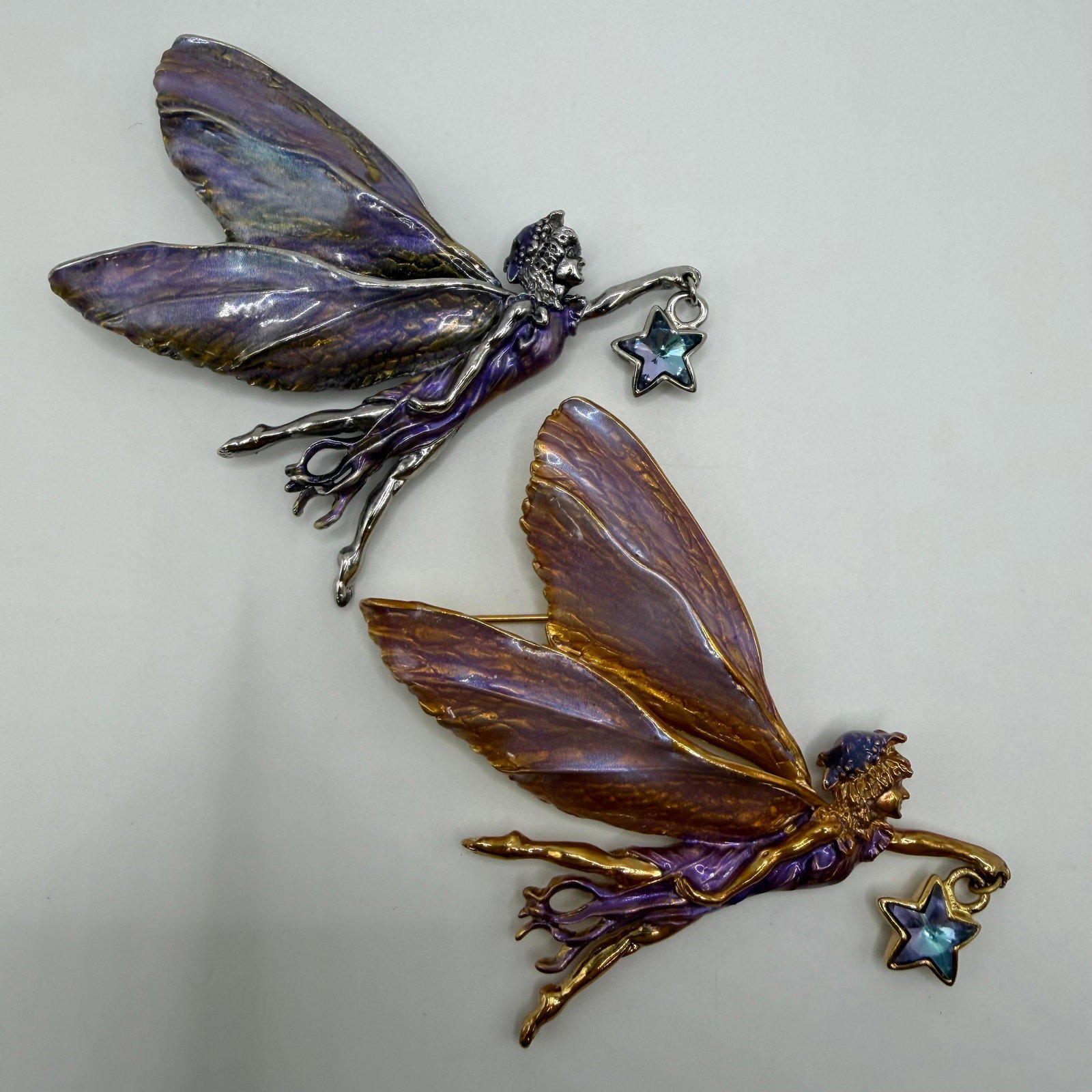 Pair of Kirks Folly Astral Fairy Enamel Brooches with Crystal Star Charms: Pair of whimsical Kirks Folly fairy brooches from the Astral collection. Includes one silver-tone and one gold-tone example, each featuring hand-painted iridescent purple enamel wings and a dangling f