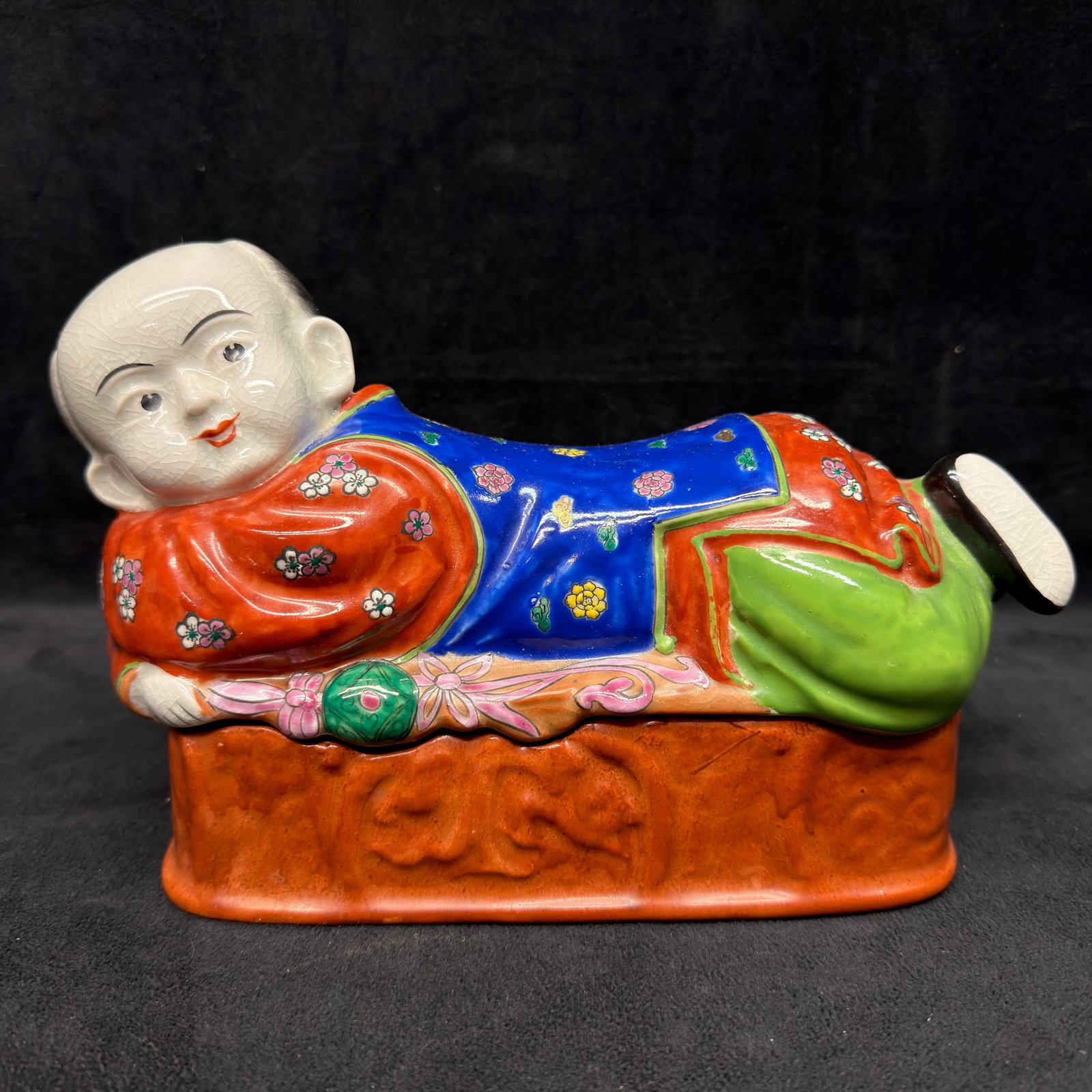 Hong Horizons Chinese Porcelain Reclining Child Covered Trinket Box: Vintage Hong Horizons Chinese porcelain covered trinket box in the form of a reclining child wearing brightly enameled traditional robes with floral decoration. The removable base provides interior st