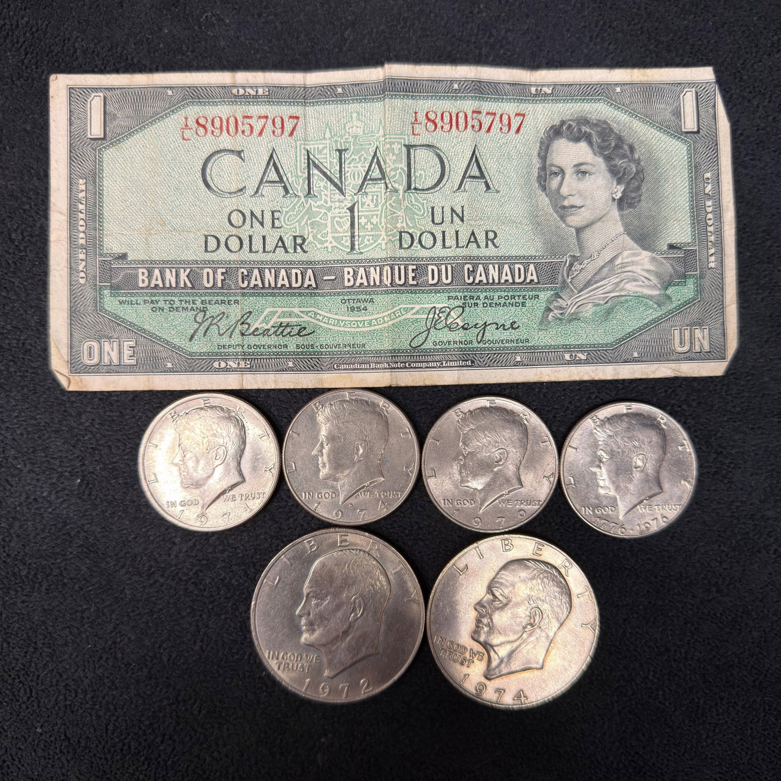 Mixed US Eisenhower Dollar Kennedy Half Dollar and Canadian Banknote Lot: Mixed lot featuring a vintage Canadian 1954 One Dollar banknote (serial L8905797), three Kennedy Half Dollars (1971, 1974, and 1979), two Eisenhower Dollars (1972, 1974), and a 1976 Bicentennial Kenne
