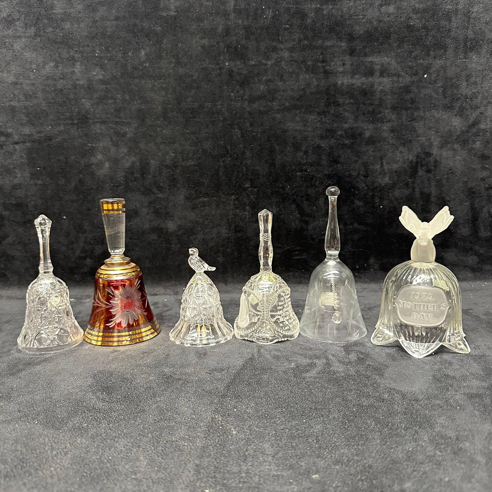 Group of Decorative Glass Bells Assorted Styles: A group of decorative glass bells in assorted styles and finishes. Includes clear pressed glass examples, etched and molded designs, figural finials, and one amber-toned bell with gilt decoration. Som