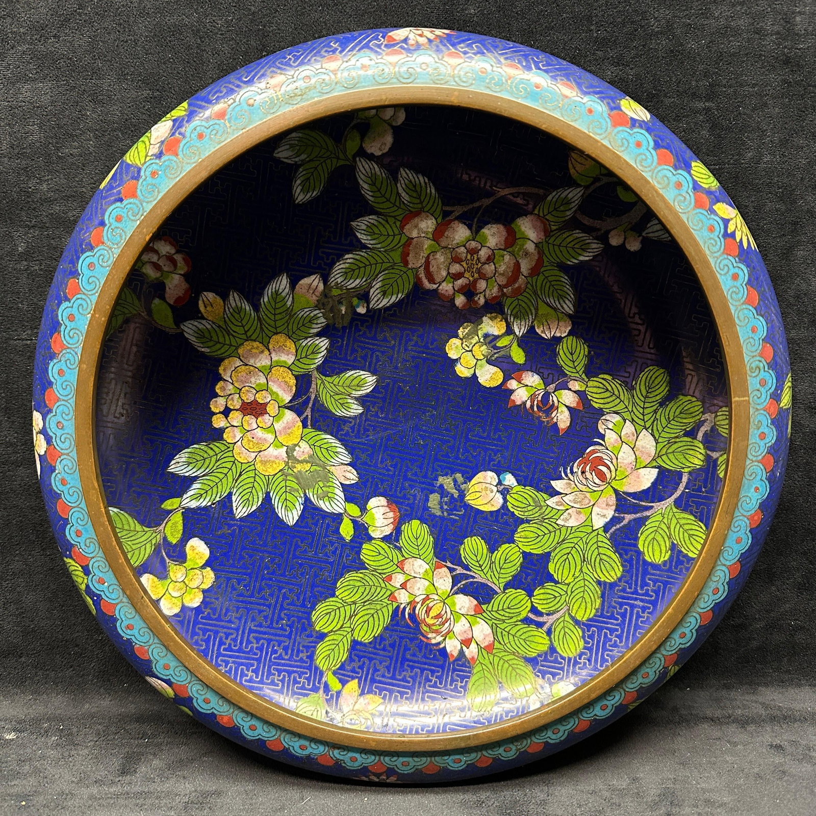 Chinese Cloisonne Enamel Floral Bowl Cobalt Blue Brass Rim: Chinese cloisonne enamel bowl featuring a deep cobalt blue ground with intricate floral and foliate designs throughout. Interior and exterior decorated with multicolored enamel flowers and scrolling p
