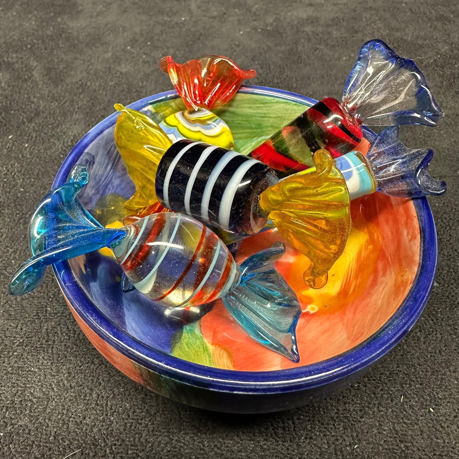 Hand Blown Art Glass Assorted Murano Style Glass Candy Figurines and Porcelain Bowl: Porcelain decorative bowl with a hand-painted floral interior and cobalt blue rim. Included are six hand-blown glass candy figurines, each with twisted ends and colorful striped and swirled designs.