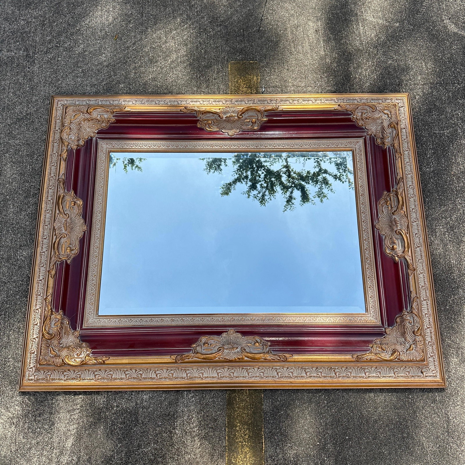 Monumental Ornate Beveled Wall Mirror in Gilt Gold and Burgundy Colored Frame: Large decorative wall mirror featuring an elaborate molded frame with gilt gold-accented scrolling, floral motifs, and deep burgundy colored lacquered panels. The mirror retains its beveled glass and 