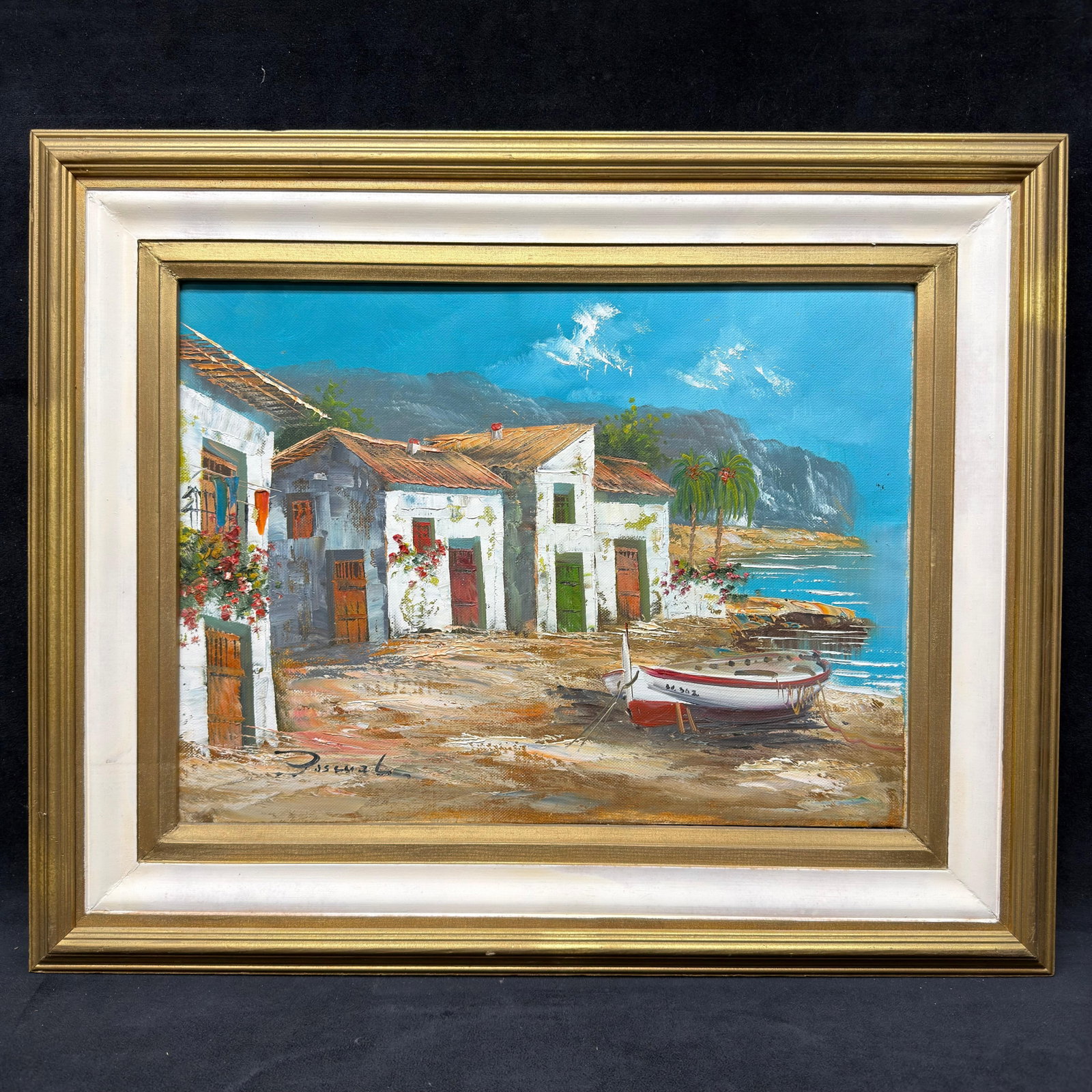 Signed Coastal Mediterranean Village Framed Oil Painting on Canvas: Original oil on canvas depicting a Mediterranean coastal village with whitewashed homes, fishing boats, palm trees, and dramatic mountains overlooking the shoreline. Signed lower left, appearing to re