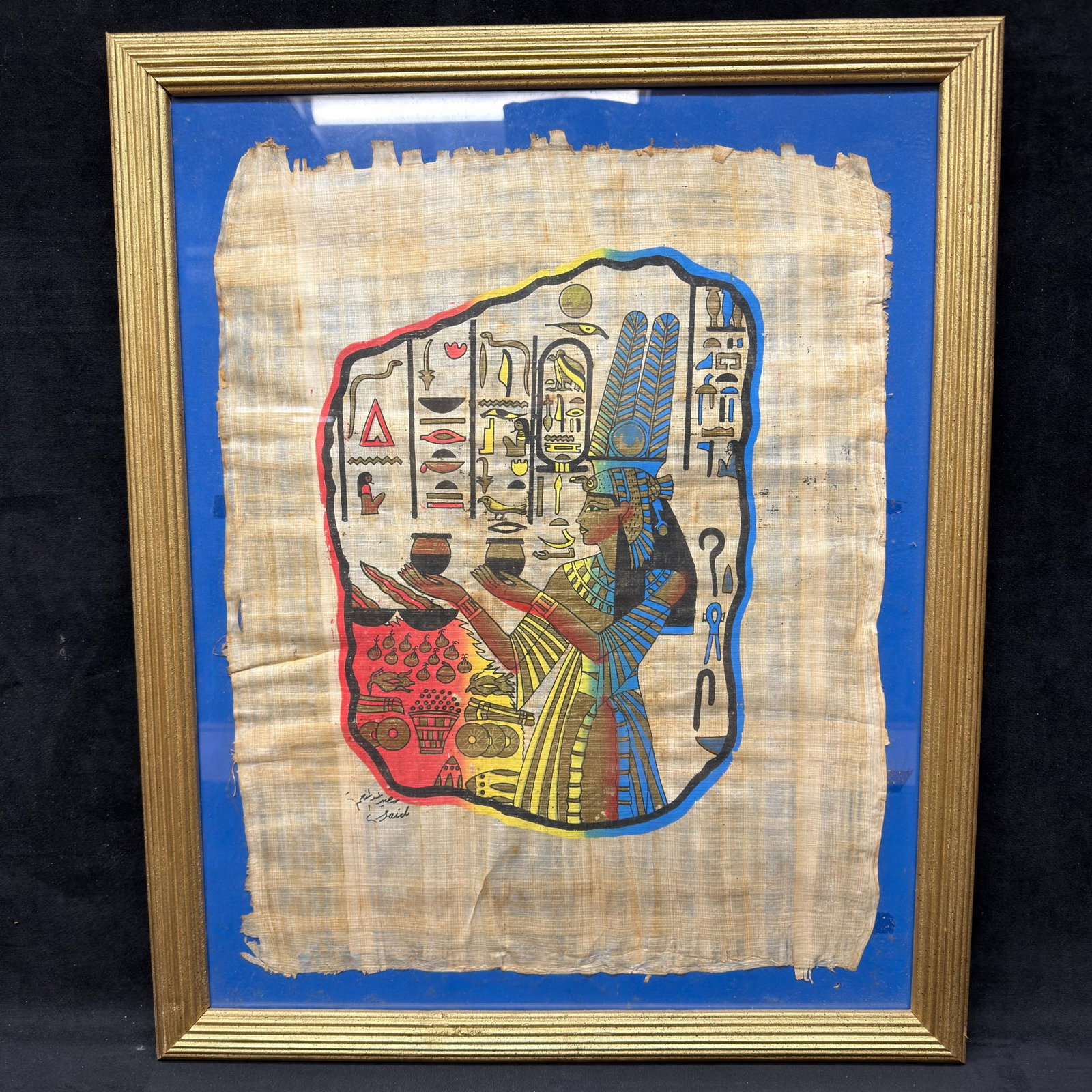 Framed Egyptian Papyrus Painting with Hieroglyphics: Hand-painted Egyptian-style scene on papyrus depicting a seated royal or deity figure presenting offerings, surrounded by colorful hieroglyphic symbols. Signed in Arabic at the lower left by an uniden