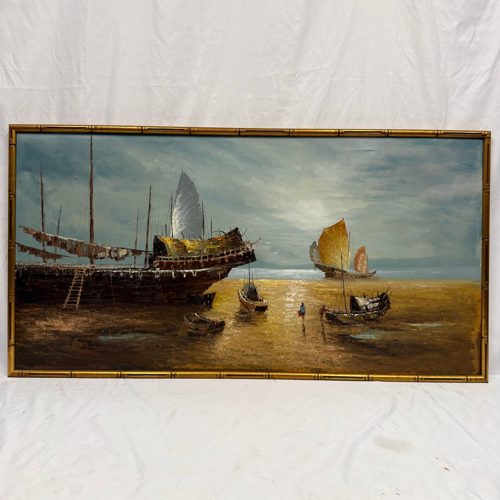 Large Harbor Seascape Oil on Canvas Gilt Bamboo Frame Junk Boats Fishing Vessel: Large vintage oil on canvas artwork depicting a tranquil harbor scene with traditional sailing vessels, junk boats resting at low tide beneath a dramatic sky. No artist signature or hallmarks noticed.