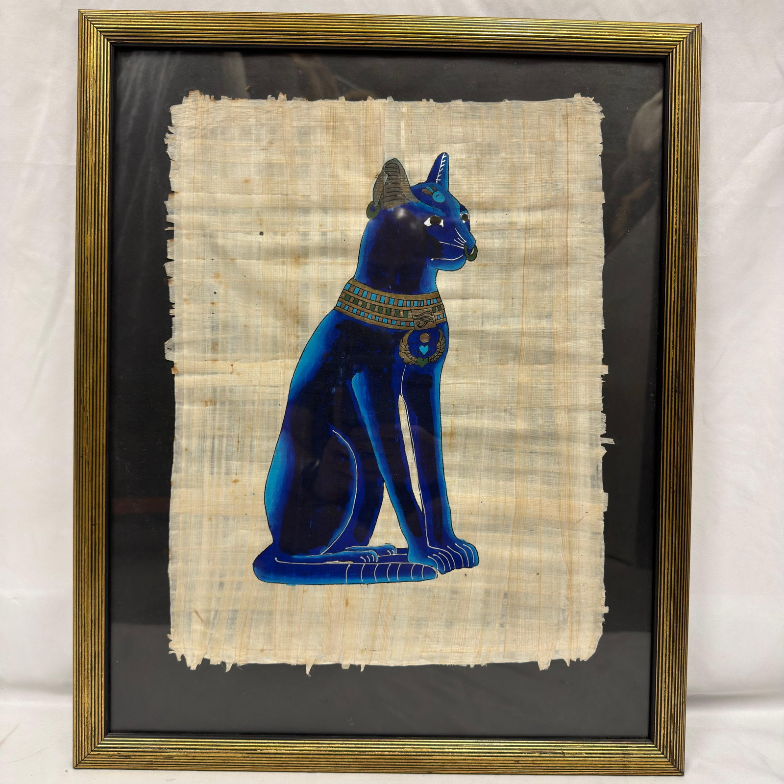 Framed Egyptian Bastet Cat Papyrus Artwork Blue Black Tones: Decorative Egyptian-style papyrus artwork depicting Bastet, the ancient Egyptian feline goddess associated with protection, home, and fertility. The figure is rendered in vivid shades of blue with tra